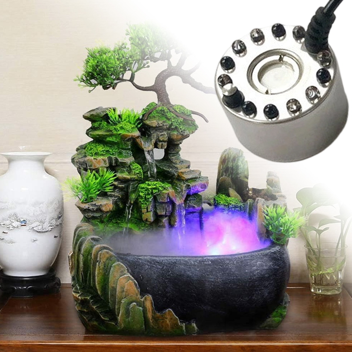 Ein dekorativer Zimmerbrunnen mit einem kleinen Baum, Felsen und Wasser. Es gibt einen Vernebler und eine Vase links.