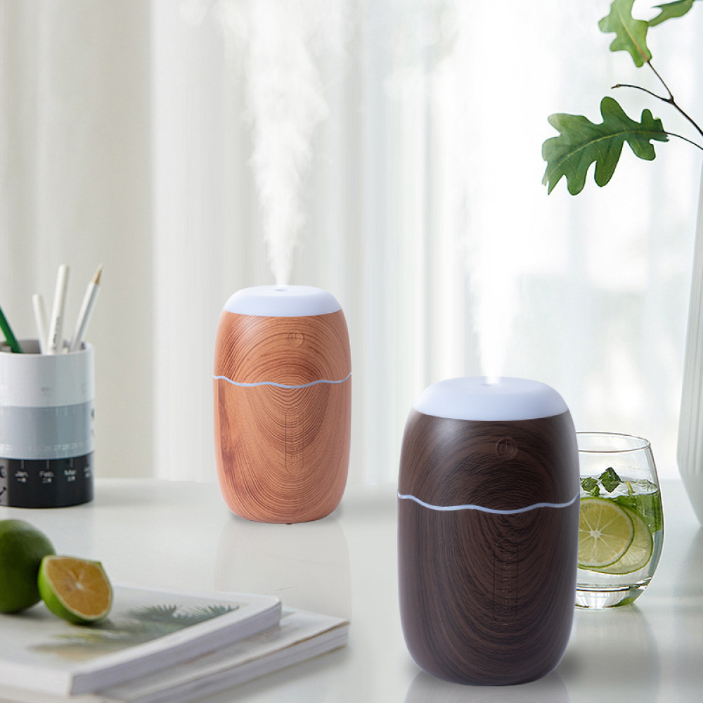 Zwei Diffusoren mit Holzmaserung, einer gibt Dampf ab. Limetten, ein Glas Wasser und ein Stifthalter stehen auf einem weißen Tisch.