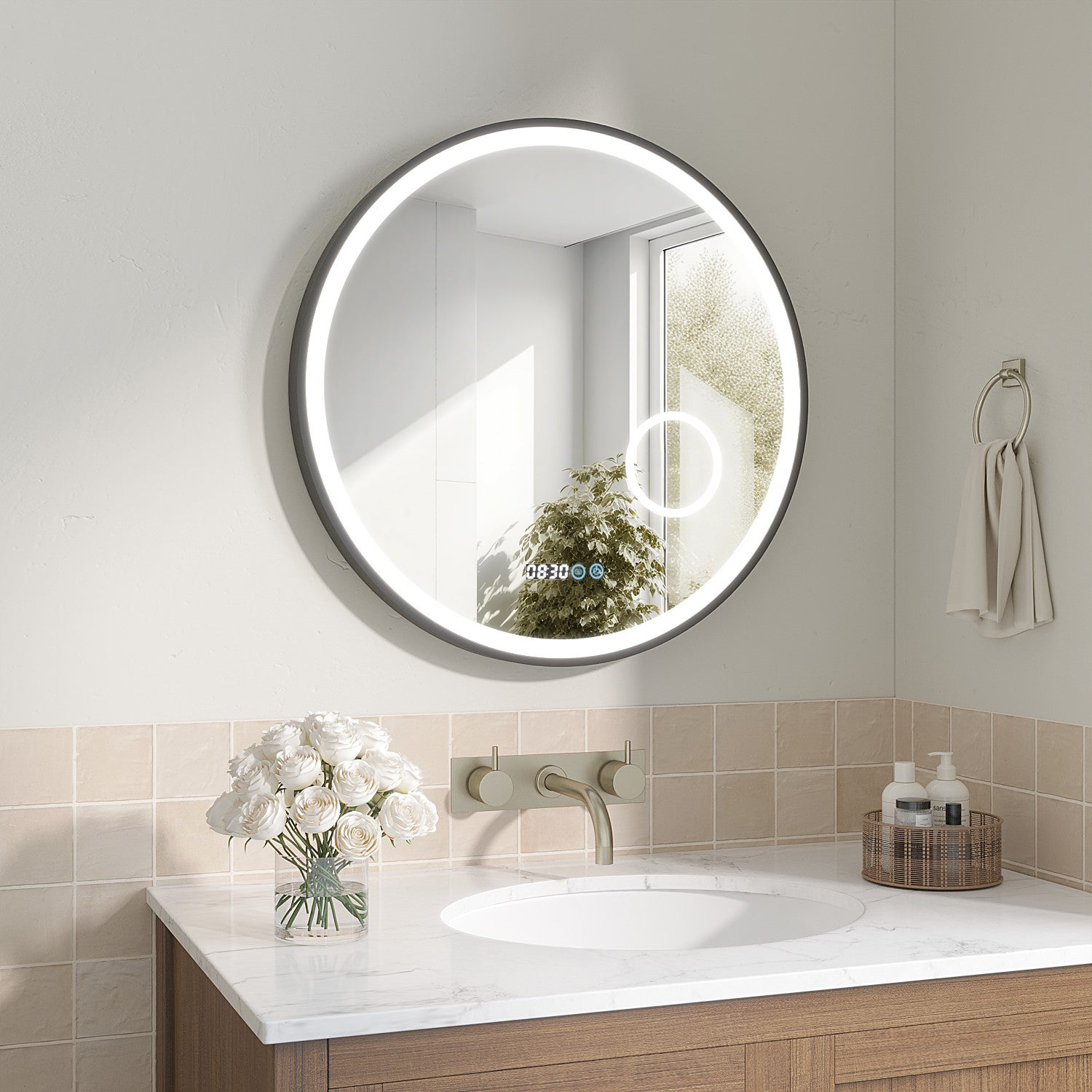 Ein modernes Badezimmer mit rundem, beleuchtetem Spiegel. Ein Waschbecken mit Blumen und Toilettenartikeln auf der Theke, Handtuch an einem Rack.