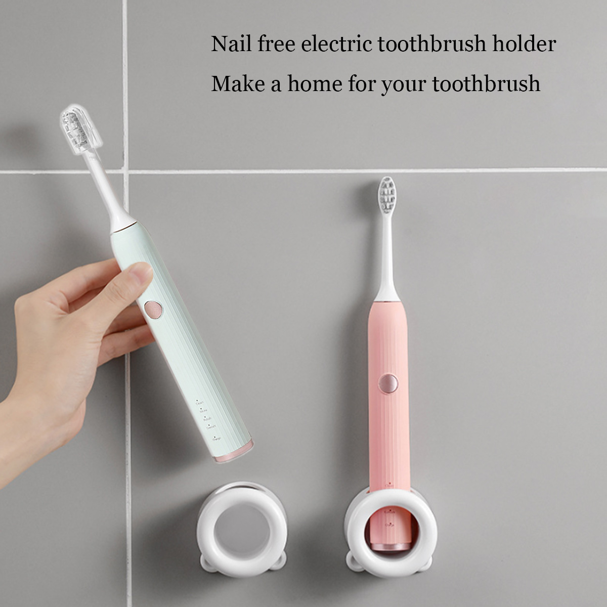 Zwei elektrische Zahnbürsten, grün und rosa, an einer grauen Wand. Eine wird von einer Hand gehalten. Halterungen unten.