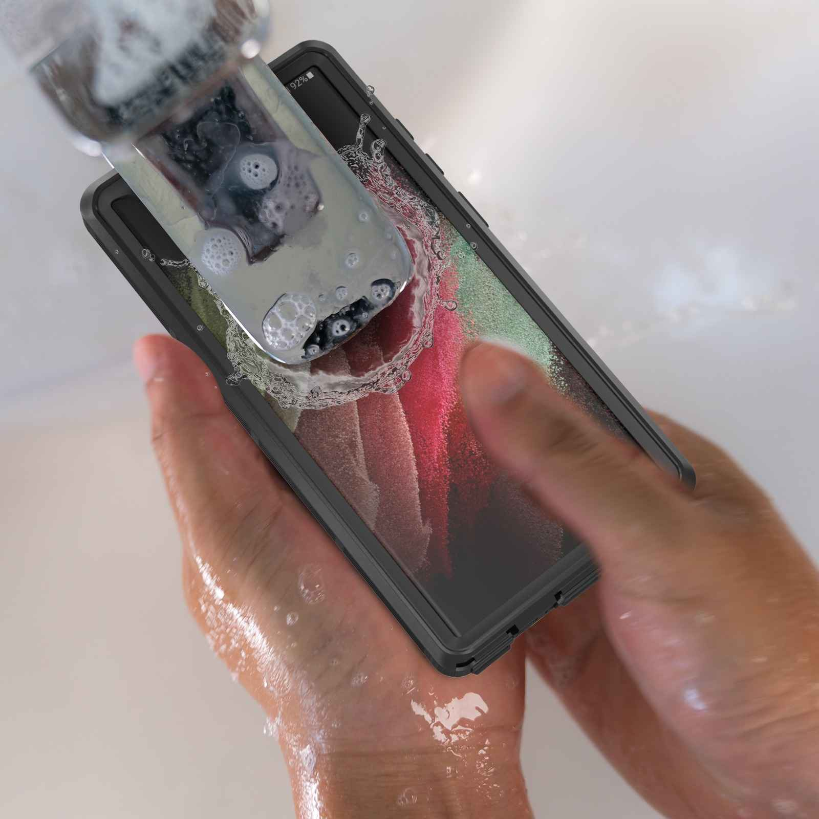 Ein Telefon in einer Hülle wird unter fließendem Wasser gehalten. Blasen und Wassertropfen sind sichtbar. Der Bildschirm zeigt Farben.