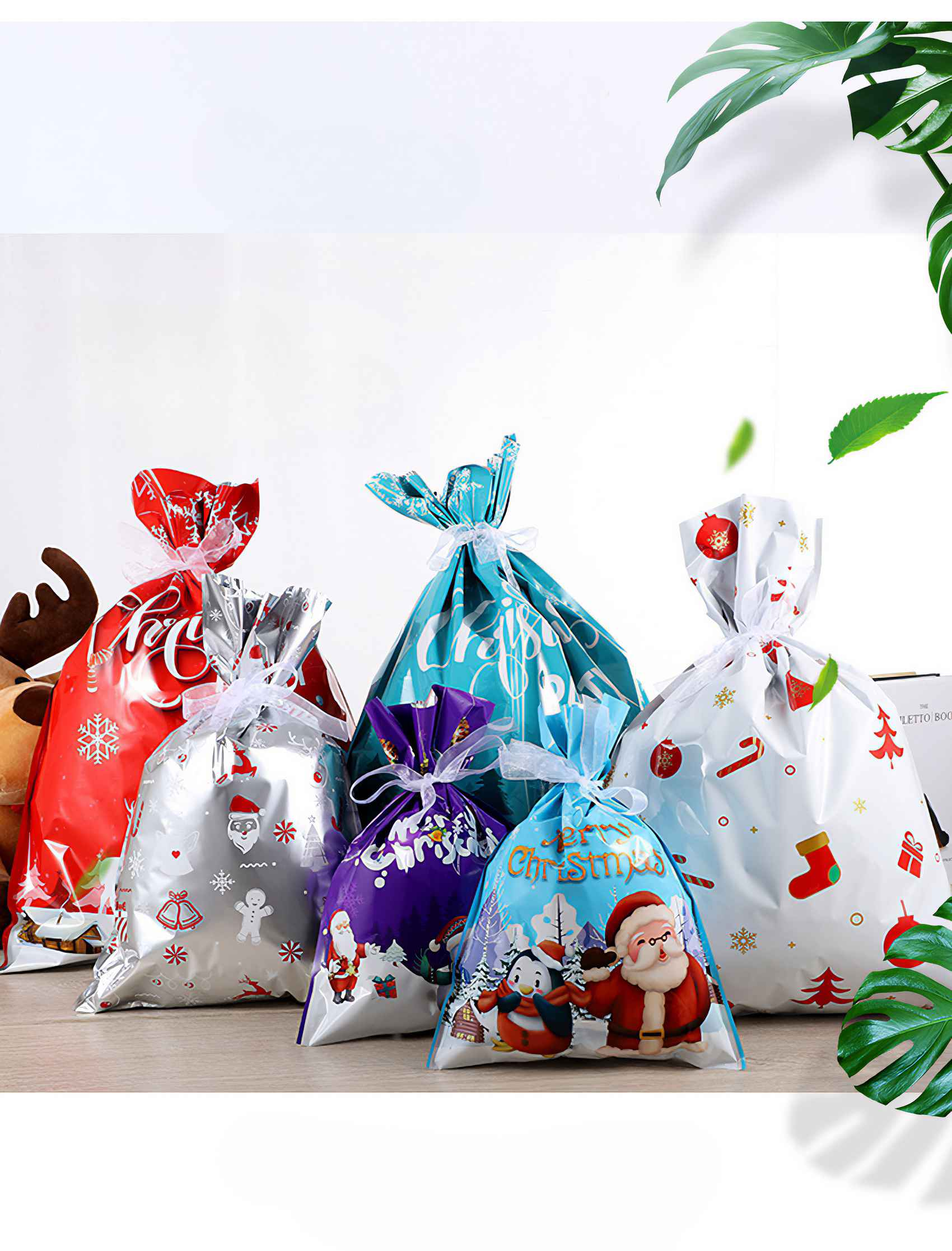 Weihnachtsgeschenktüten in Rot, Blau, Weiß und Lila mit festlichen Designs und weißen Schleifen auf einer Holzoberfläche.