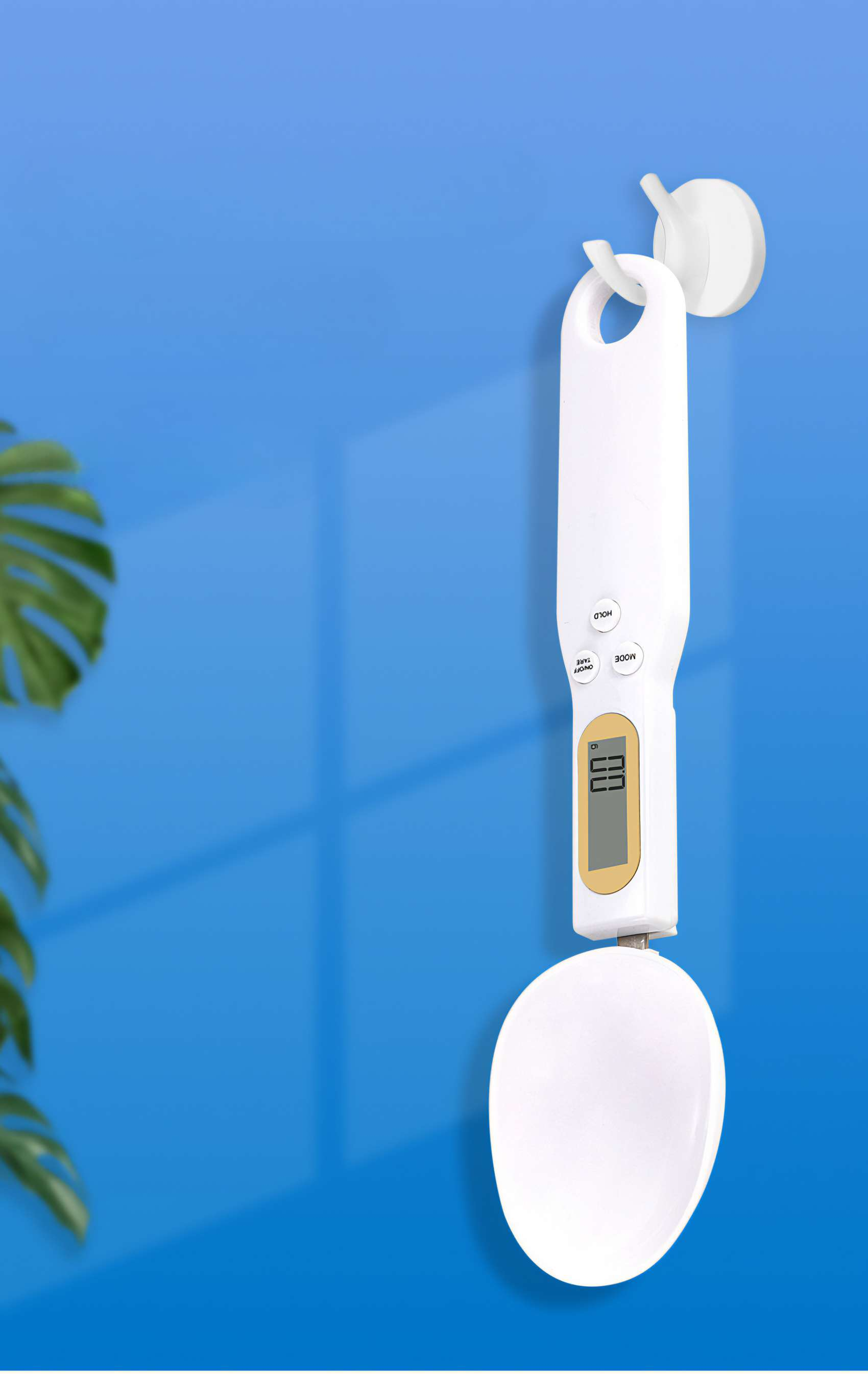 Eine weiße digitale Küchenwaage hängt an einer blauen Wand. Sie hat ein löffelförmiges Design.
