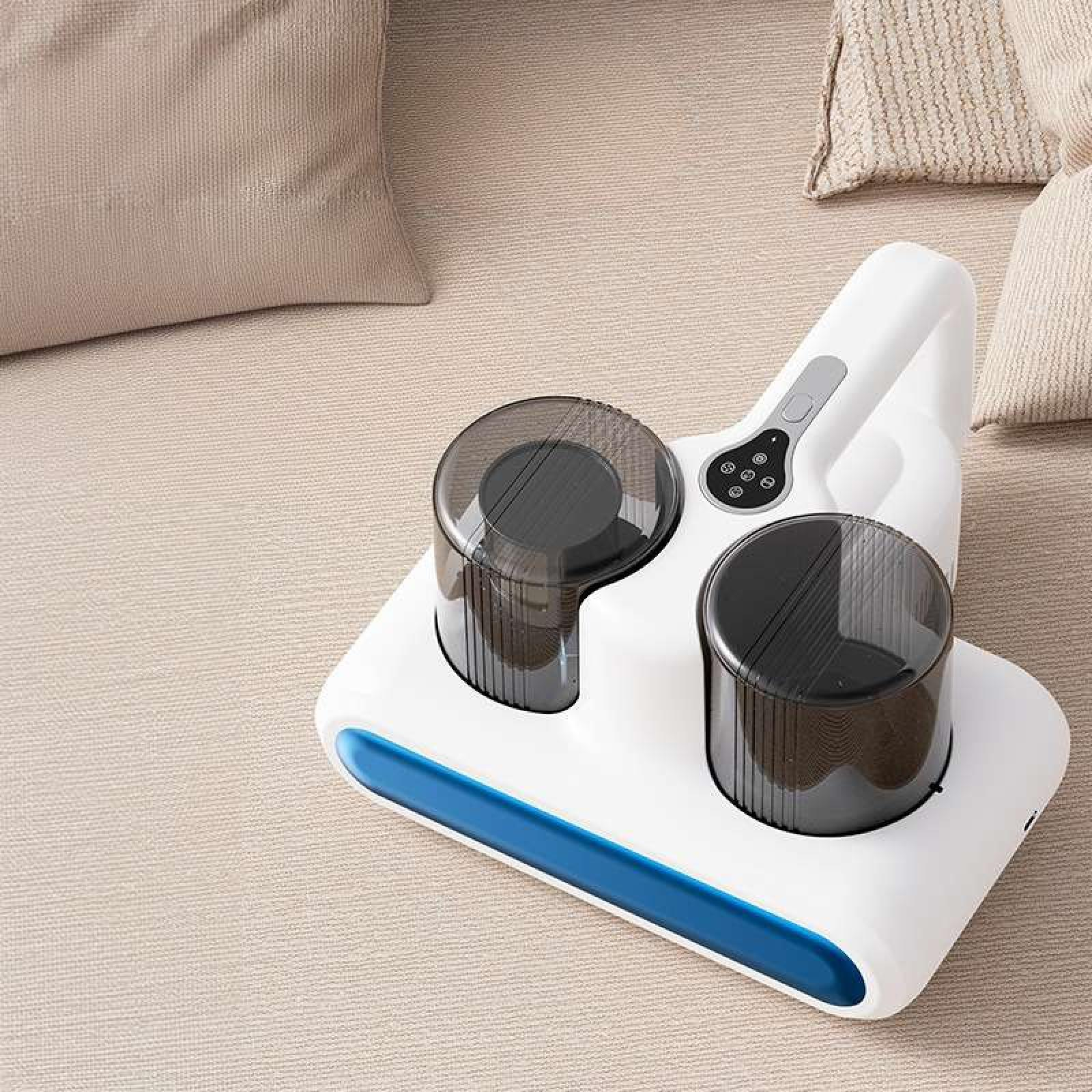 Ein weiß-blauer Staubsauger mit zwei schwarzen Behältern, platziert auf einer beigefarbenen Oberfläche mit Kissen.