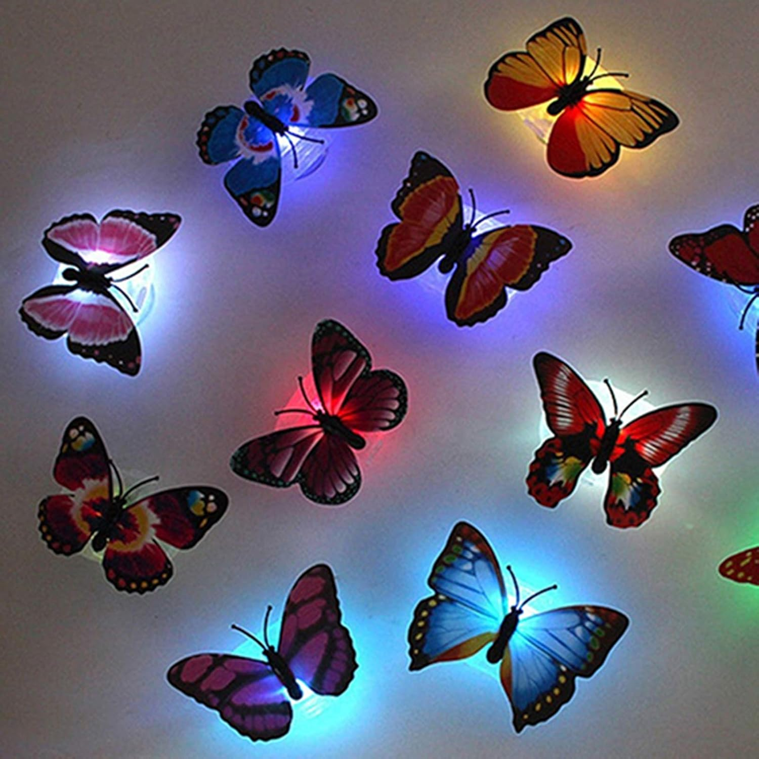Mehrere leuchtende Schmetterlingsdekorationen in verschiedenen Farben sind an einer hellen Wand befestigt. Jedes strahlt sanft.