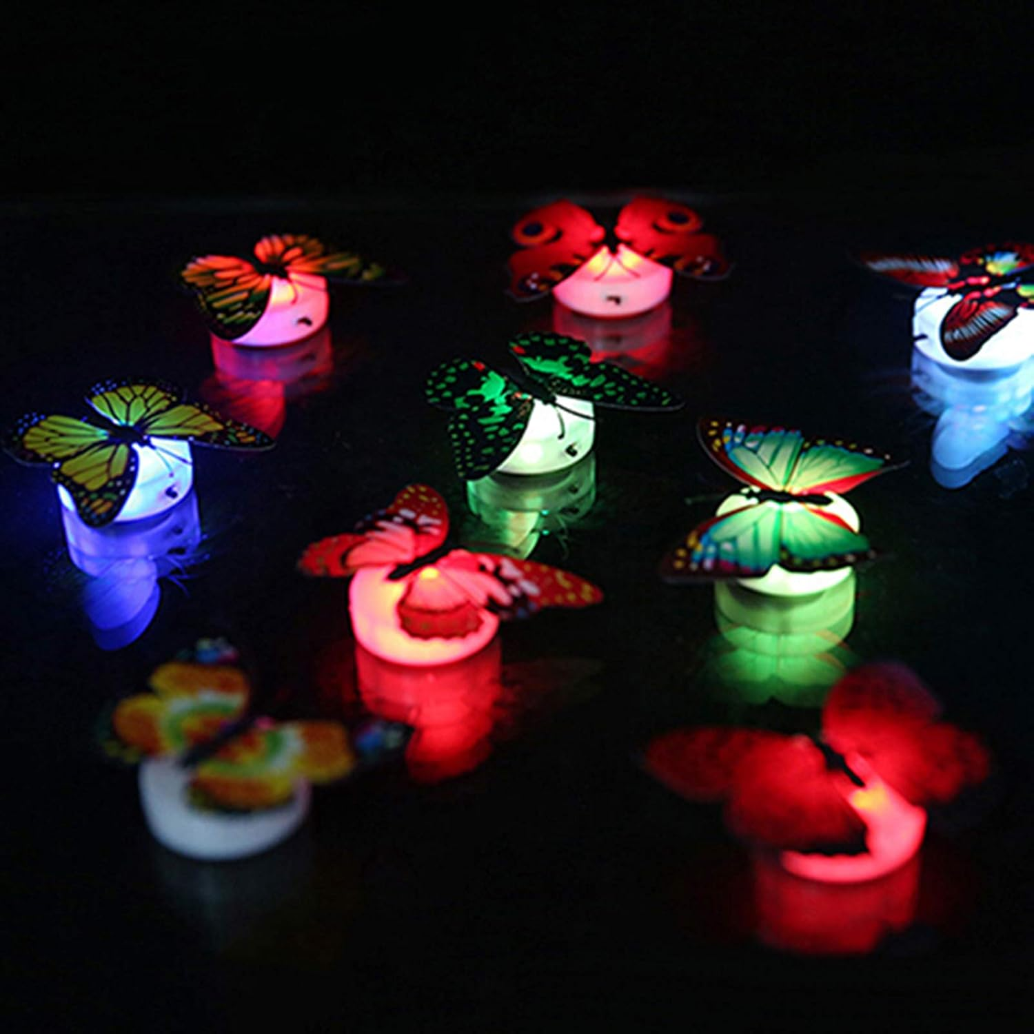 Mehrere schmetterlingsförmige Nachtlichter mit bunten Flügeln sind beleuchtet. Der Hintergrund ist dunkel, mit Reflexionen der Lichter auf einer Oberfläche.