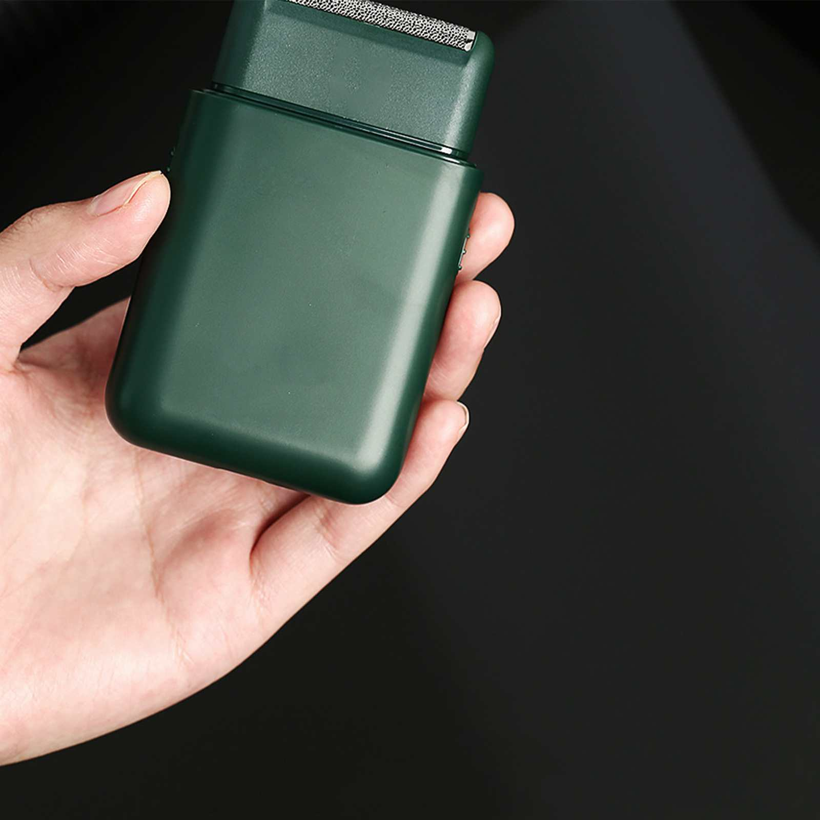 Eine Hand, die einen grünen Elektrorasierer hält. Der Hintergrund ist schwarz.