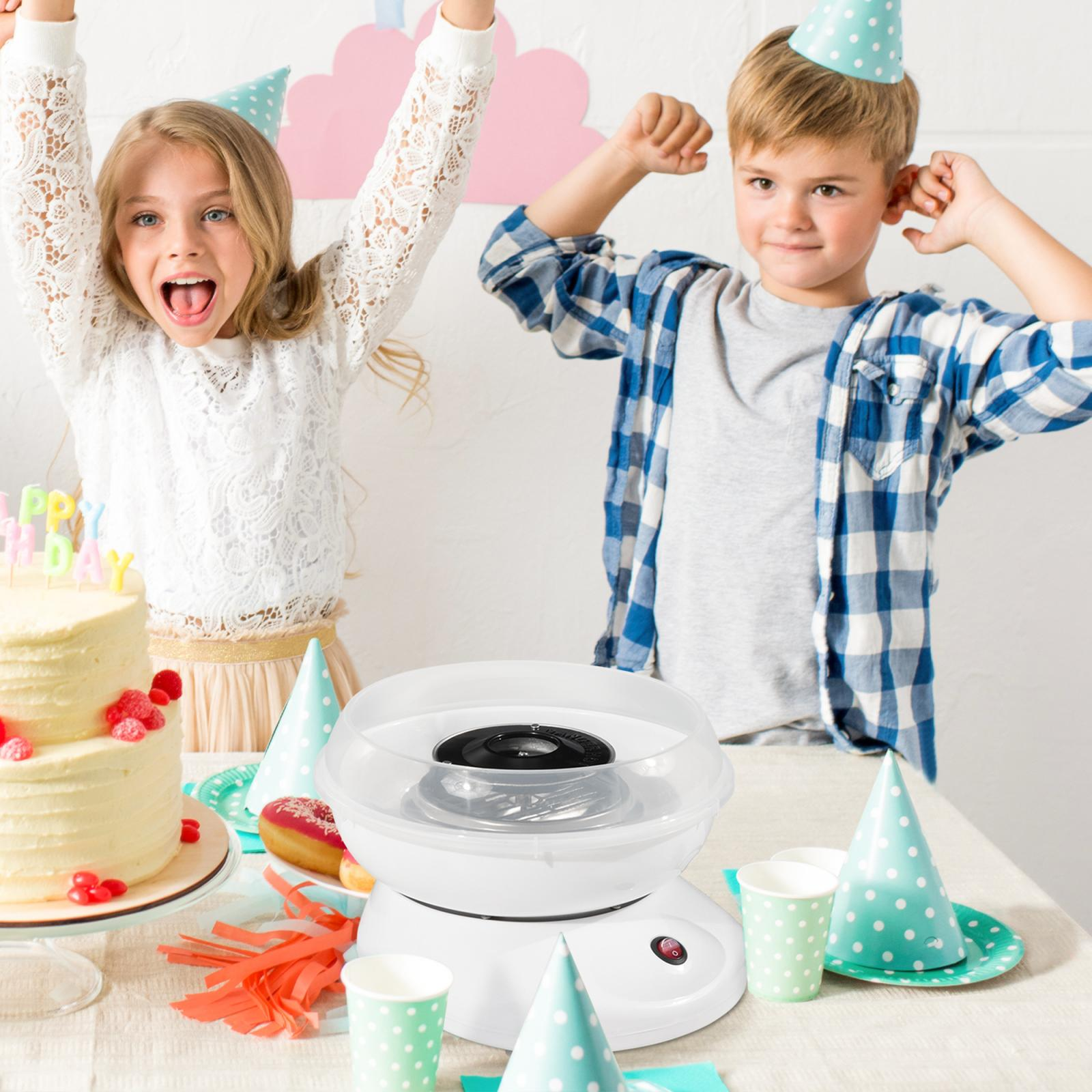 Zwei Kinder mit Partyhüten feiern. Auf einem Tisch stehen eine Zuckerwattemaschine, Kuchen und Donuts.