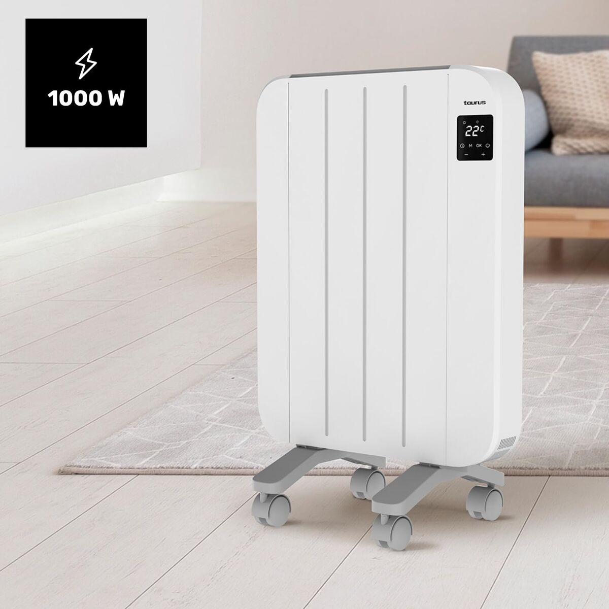 Stufa elettrica bianca con display digitale, su ruote. Potenza 1000W. Sullo sfondo, un divano grigio. Su pavimento in legno.