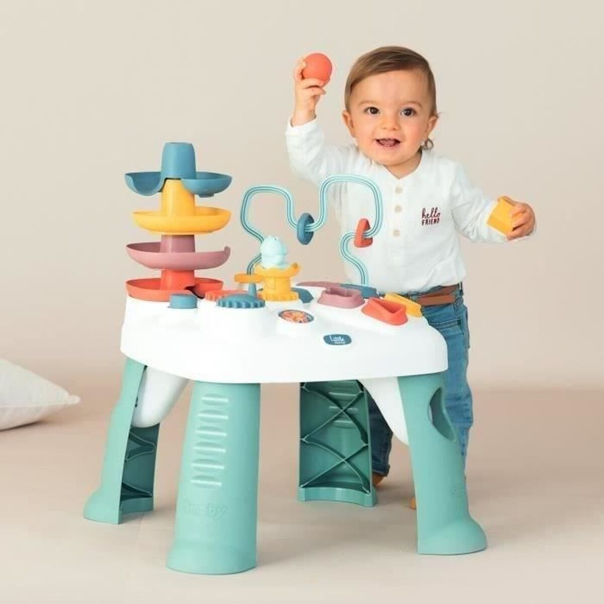 Ein Baby spielt mit einem Spieltisch. Er hat bunte Komponenten und eine Kugelbahn. Das Baby hält einen Ball und einen Block.