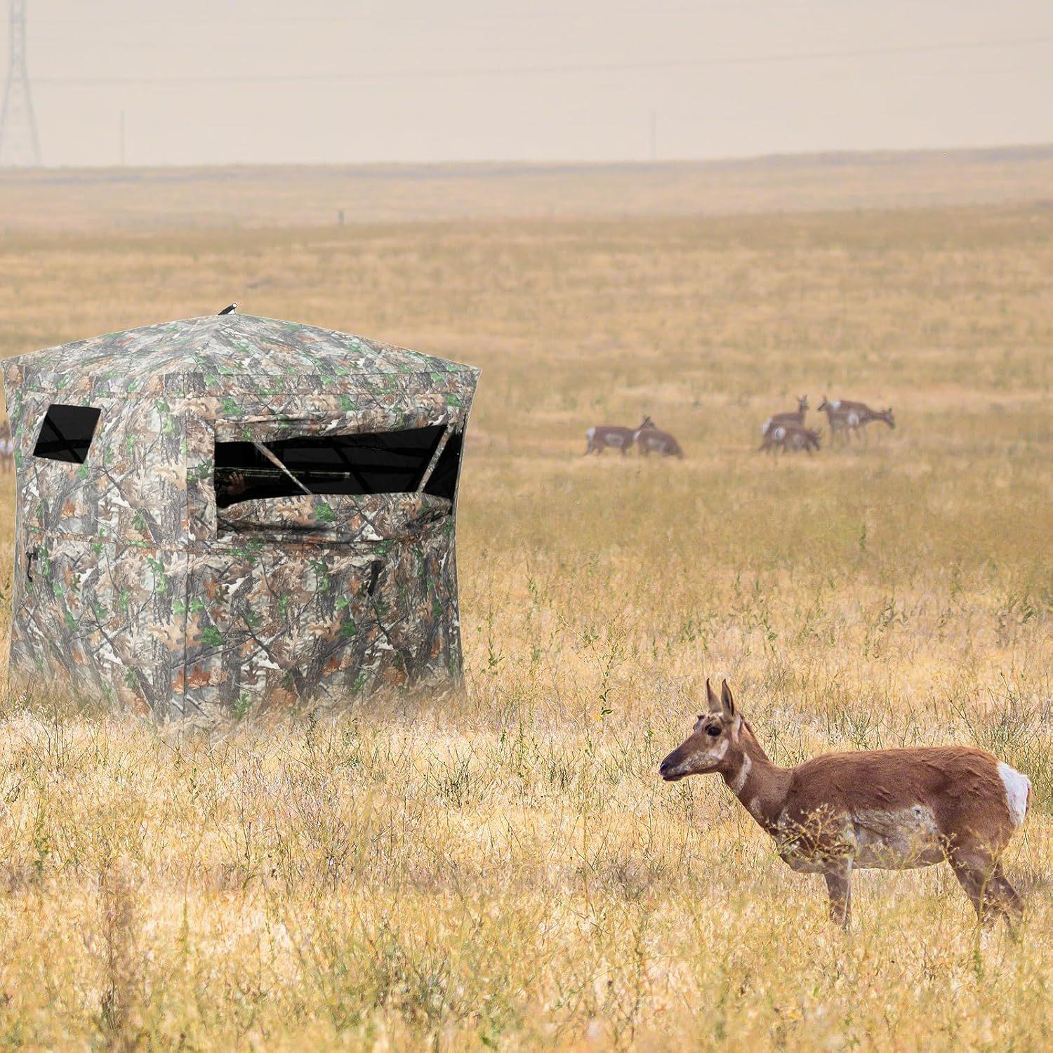 Ein Tarn-Jagdunterstand steht auf einem Feld. Ein Gabelbock steht im Vordergrund, weitere im Hintergrund.