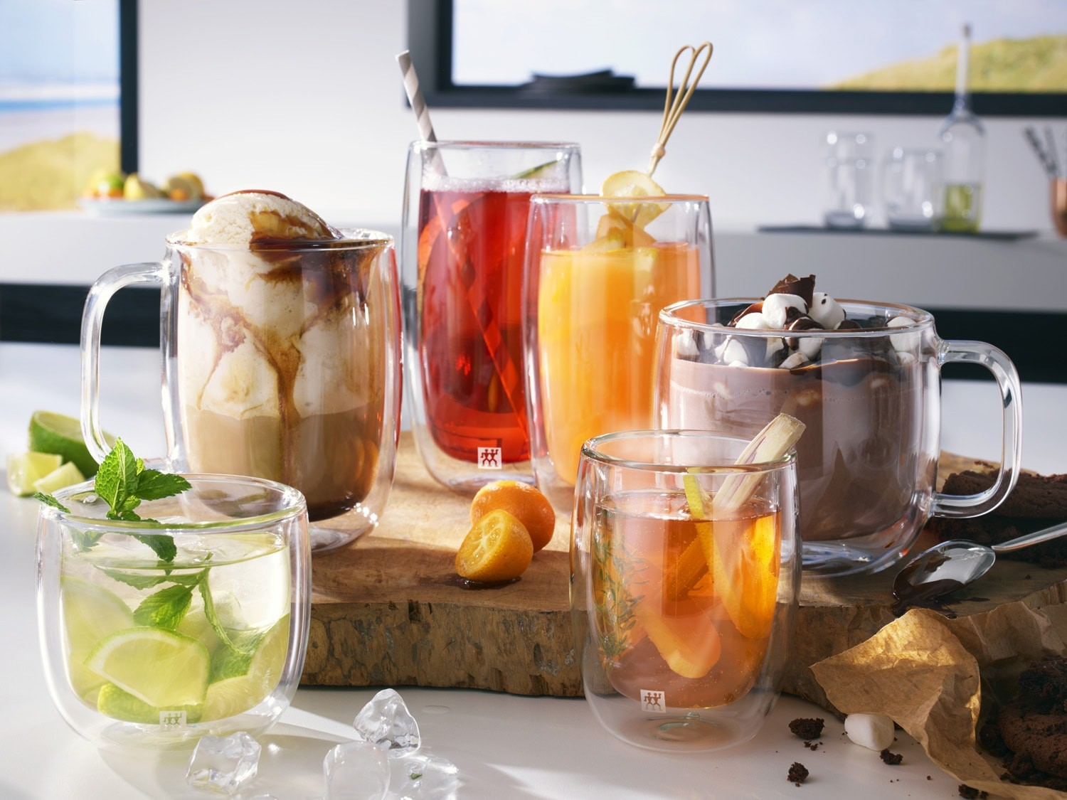 Verschiedene Getränke in Glasbechern und Gläsern. Eiscreme, Saft und Schokoladengetränke sind sichtbar. Limetten und Orangen liegen auf einem Holzbrett.