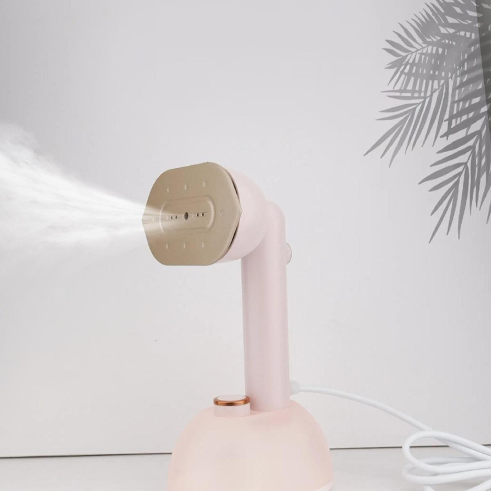 Ein rosa Handdampfer für Kleidung gibt Dampf ab. Im Hintergrund befindet sich ein Palmenblatt-Schatten an der weißen Wand.