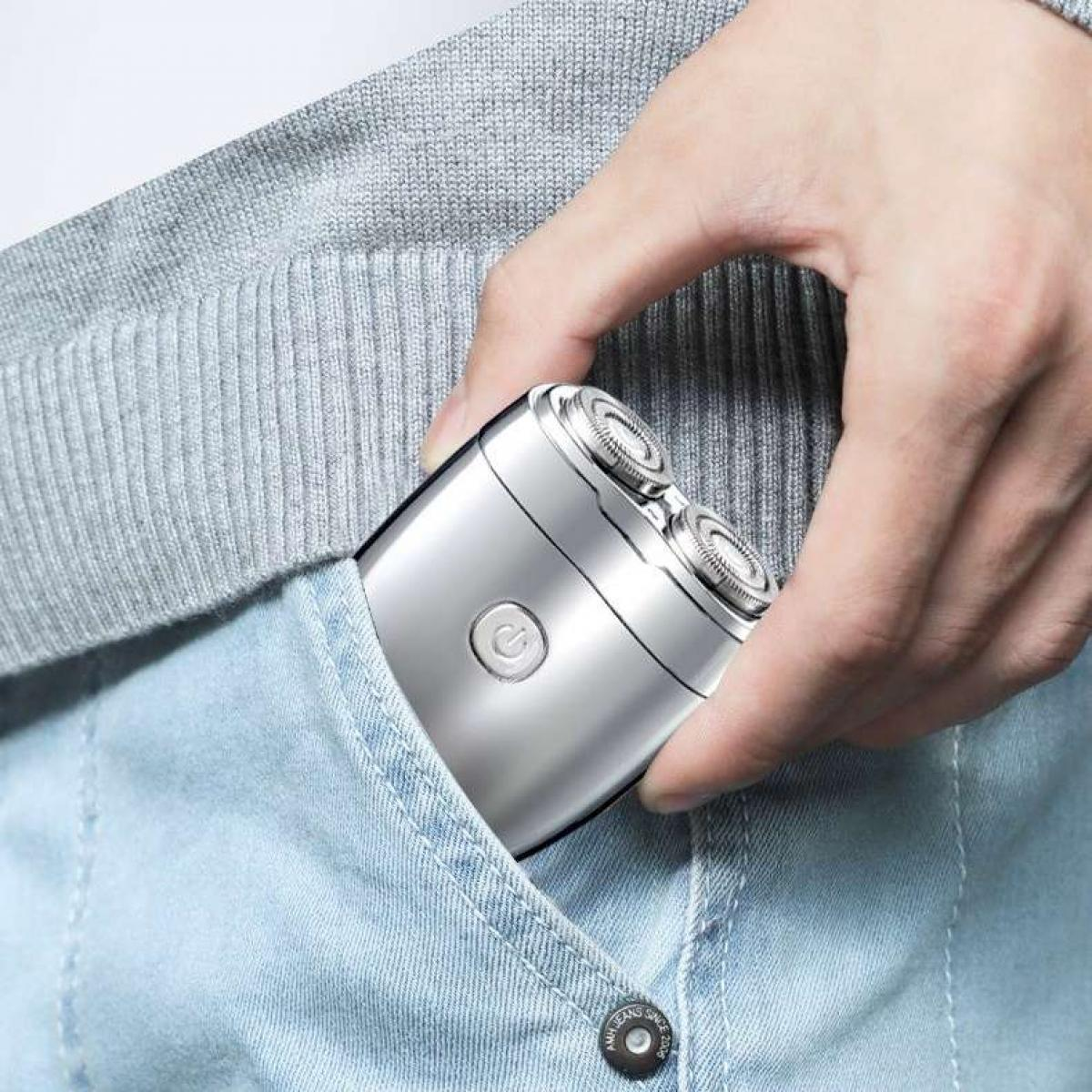 Eine Person hält einen silbernen Elektrorasierer in einer Jeans-Tasche. Im Hintergrund ist ein grauer Pullover zu sehen.