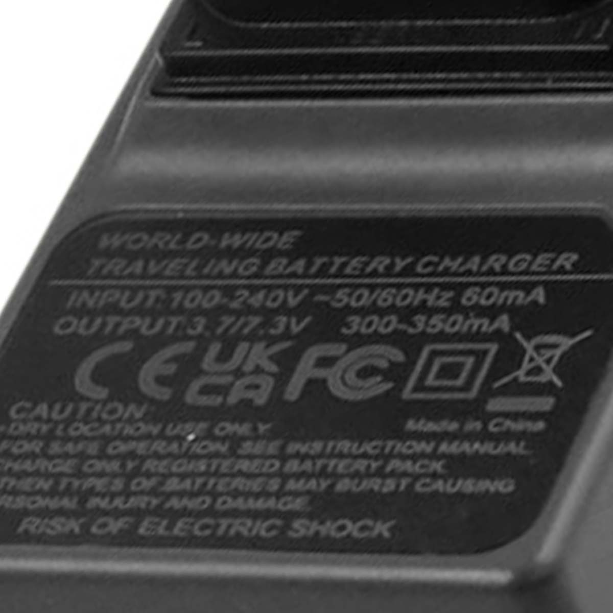 Primer plano de un cargador de batería negro con texto blanco. Dice 'World-Wide Traveling Battery Charger' y muestra especificaciones de entrada/salida.