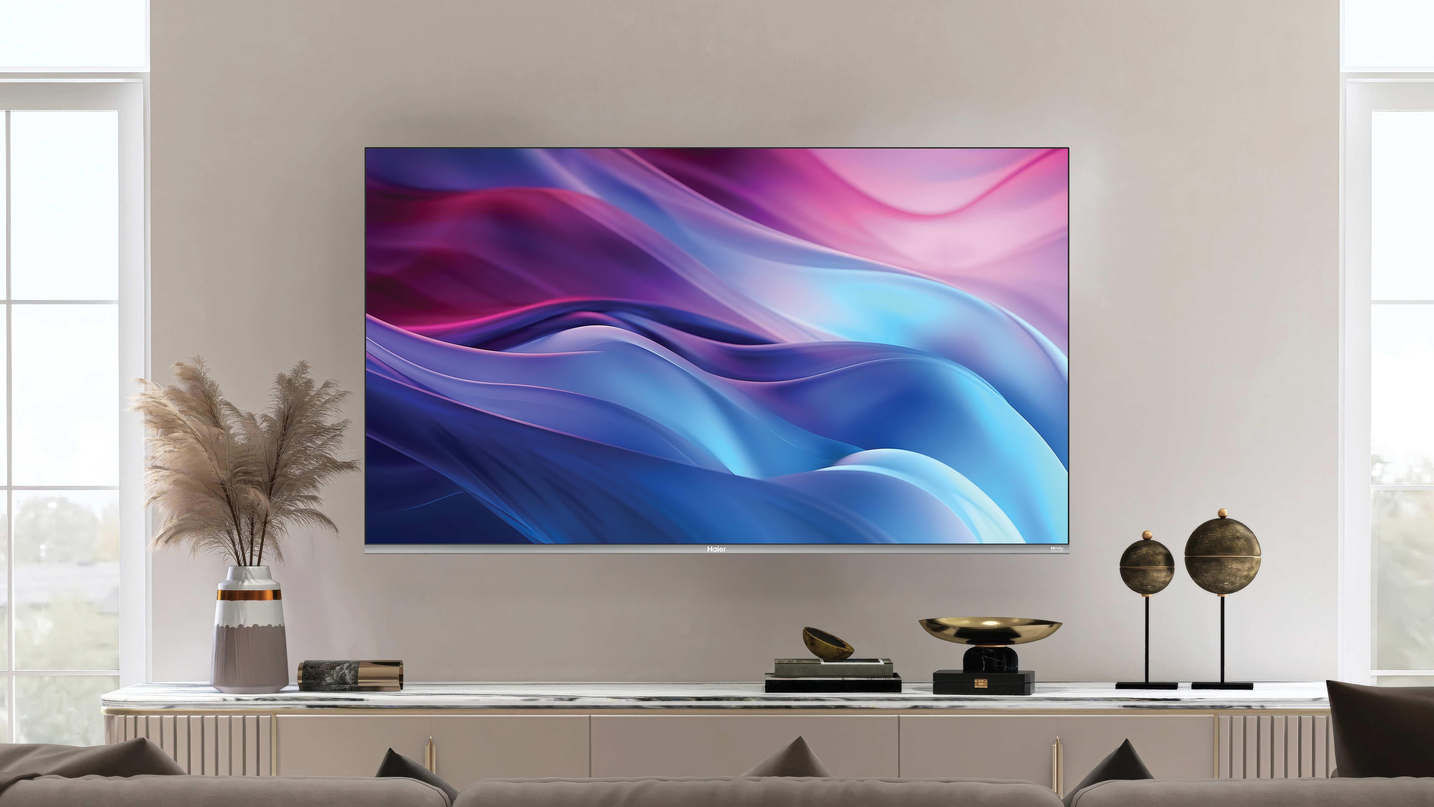 Una grande TV mostra arte astratta. Una console sottostante ha decorazioni. Un vaso contiene piante secche. Finestre su entrambi i lati.