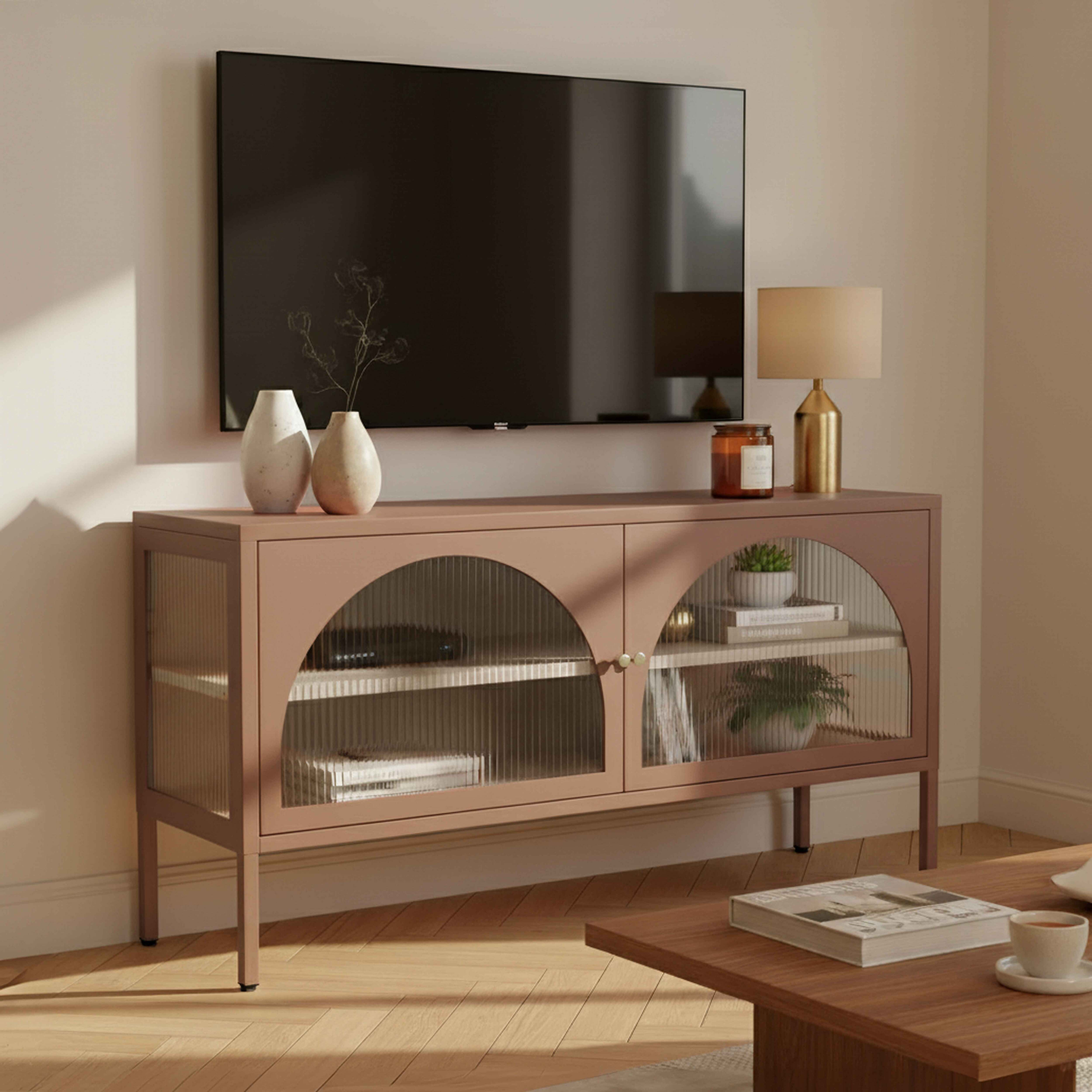 Ein Fernseher über einem rosa Schrank mit Vasen, einer Lampe und Dekor. Ein Couchtisch mit einem Buch und einer Tasse.
