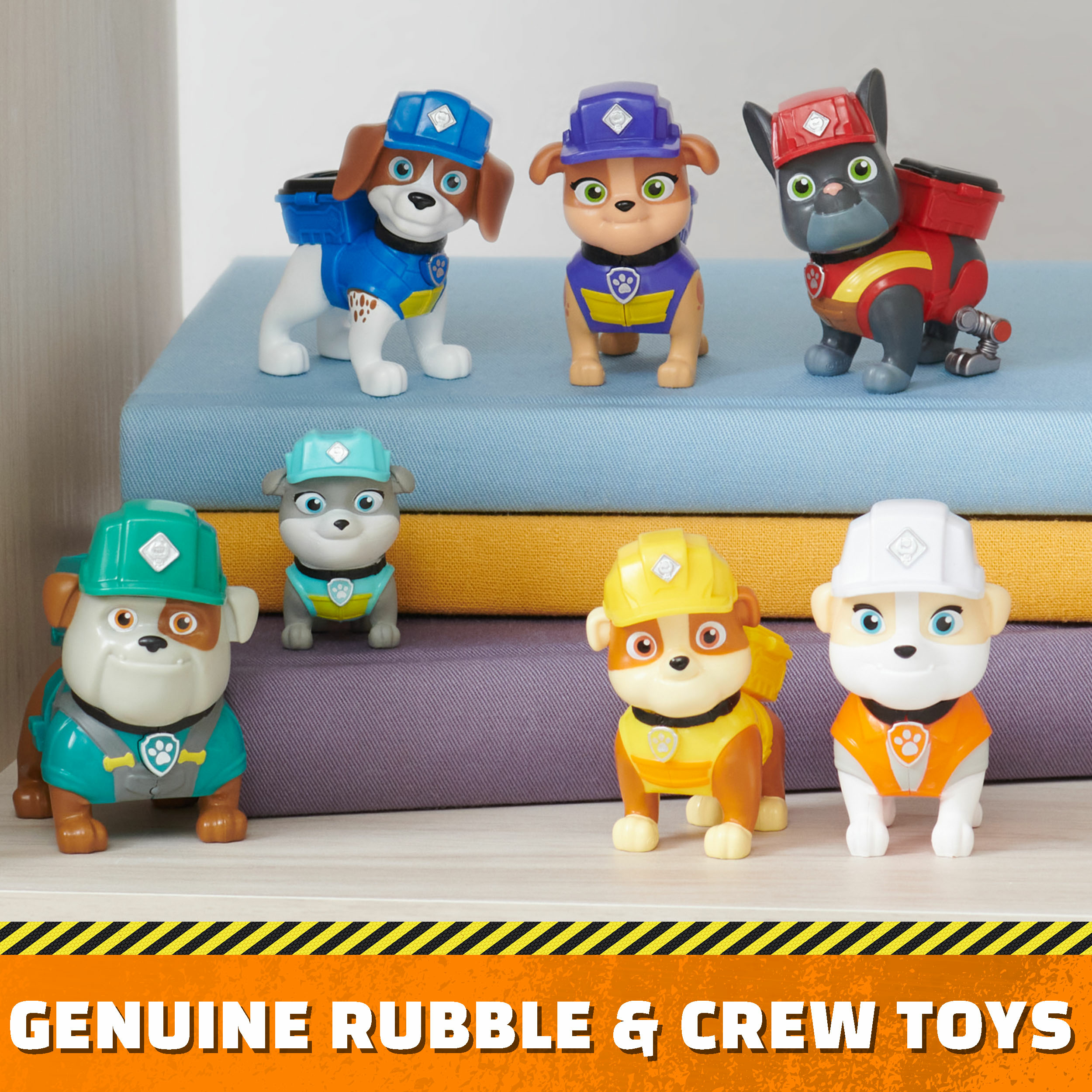 Zabawki Paw Patrol na książkach. Sześć zabawek psów w kaskach i mundurach. Poniżej napis 'Genuine Rubble & Crew Toys'.