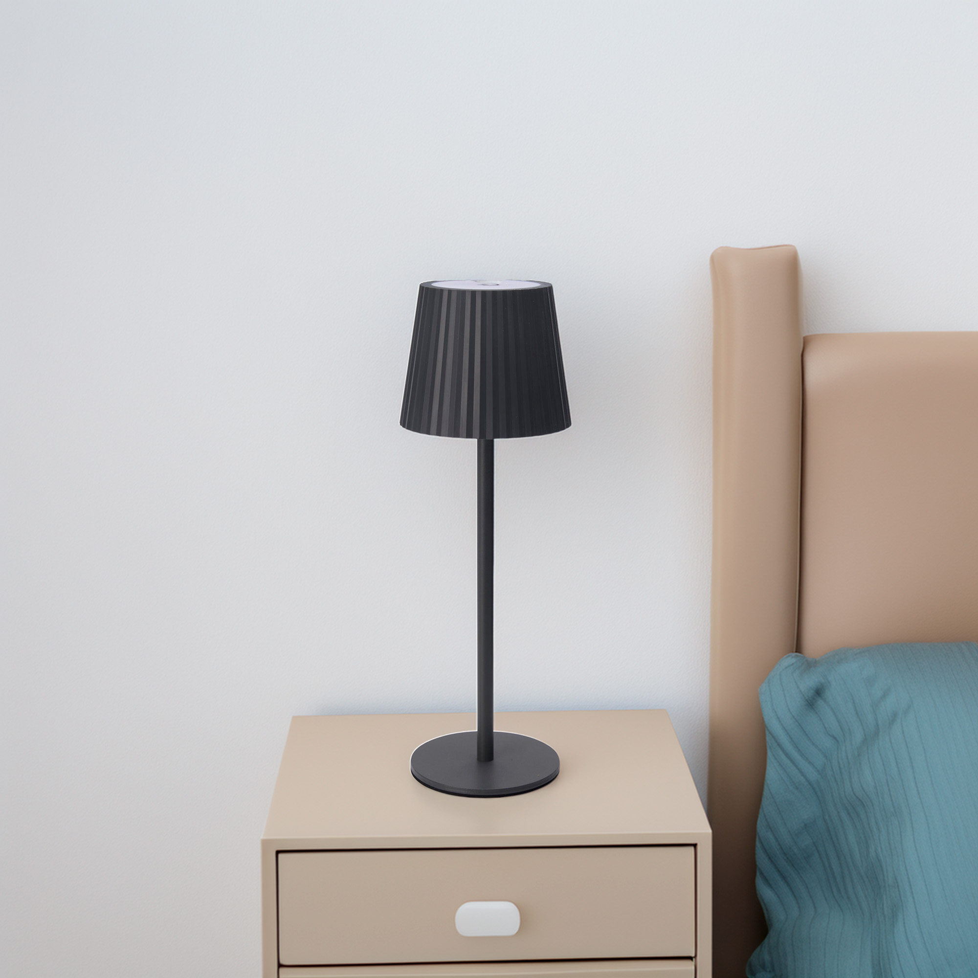 Una lámpara negra en una mesita de noche beige junto a una cama con cabecero beige y almohada azul.