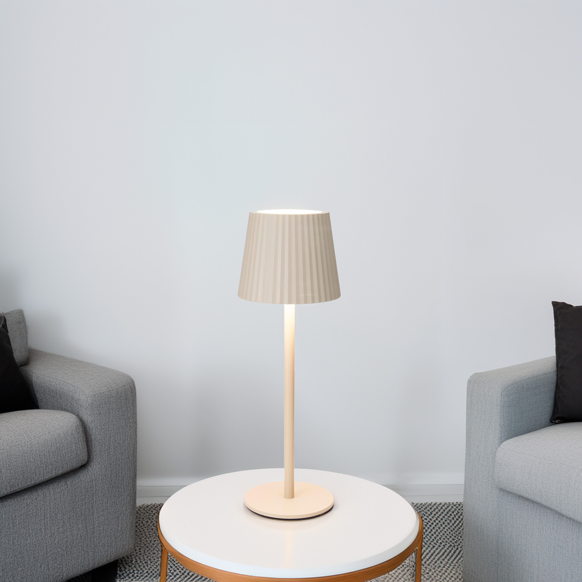 Una lámpara beige está sobre una mesa blanca entre dos sillones grises. Cojines negros en las sillas.