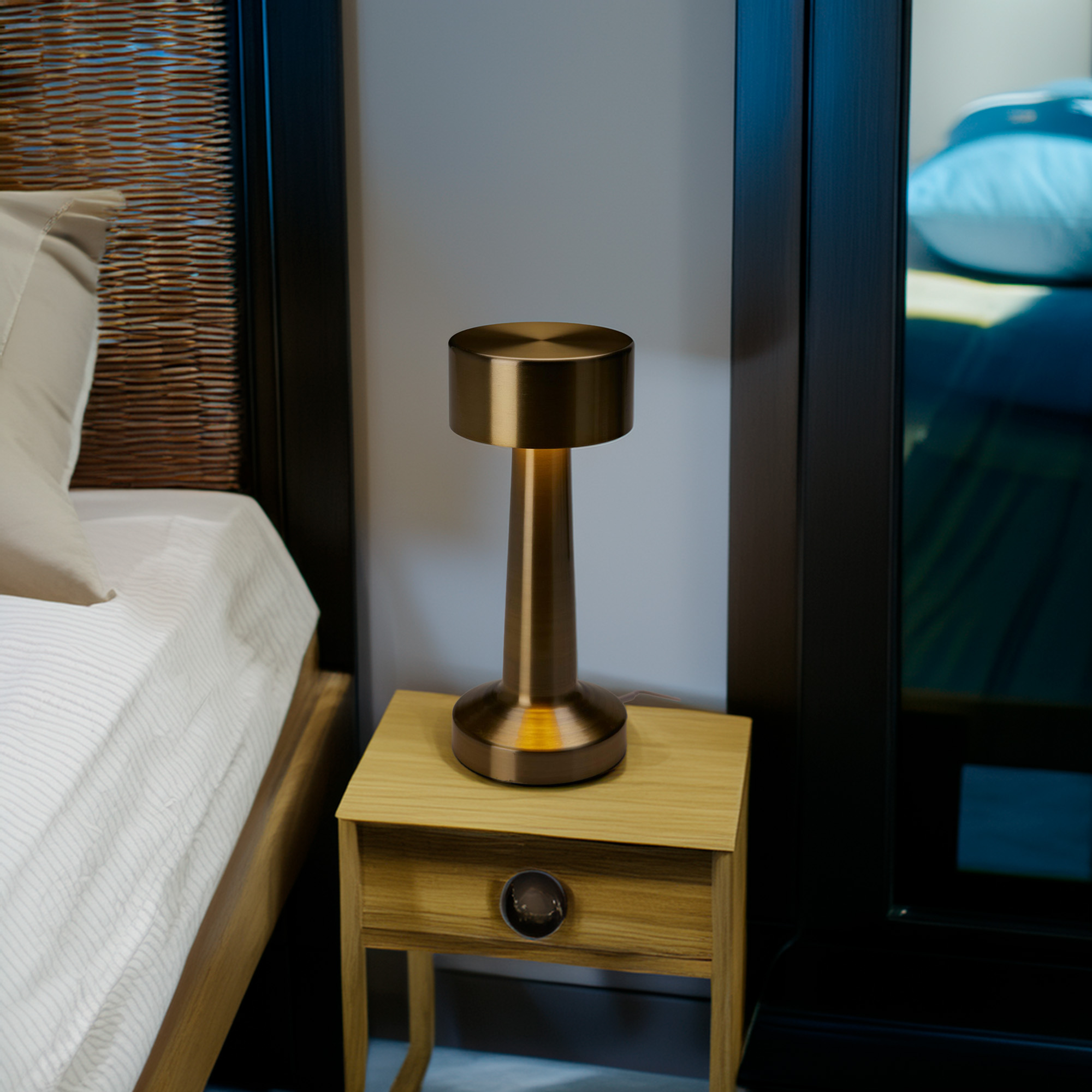 Una lámpara dorada de noche sobre una mesita de noche de madera. Cama a la izquierda, espejo a la derecha.