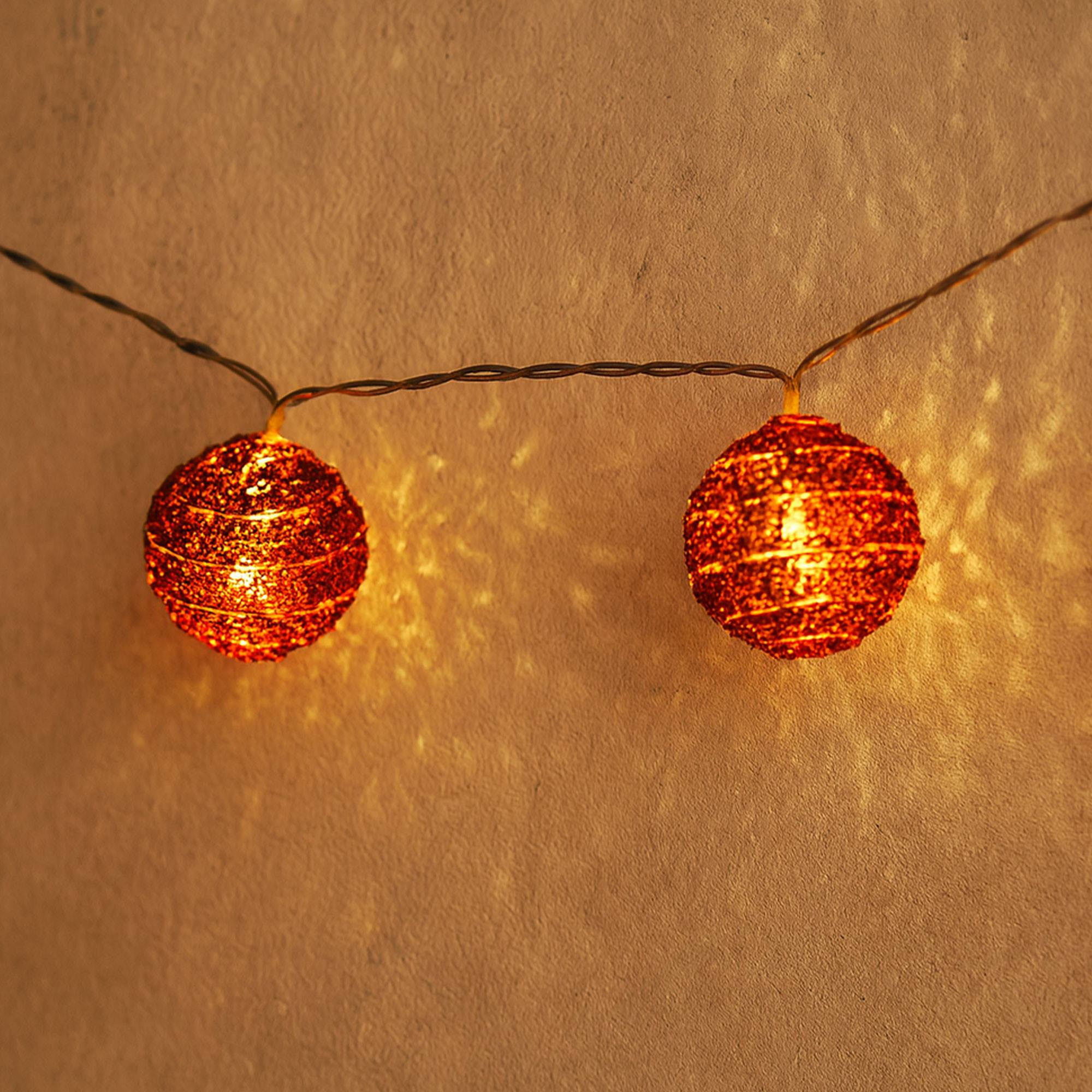 Dos luces esféricas naranjas brillantes en un cable. El fondo es una pared texturizada y de tonos cálidos.
