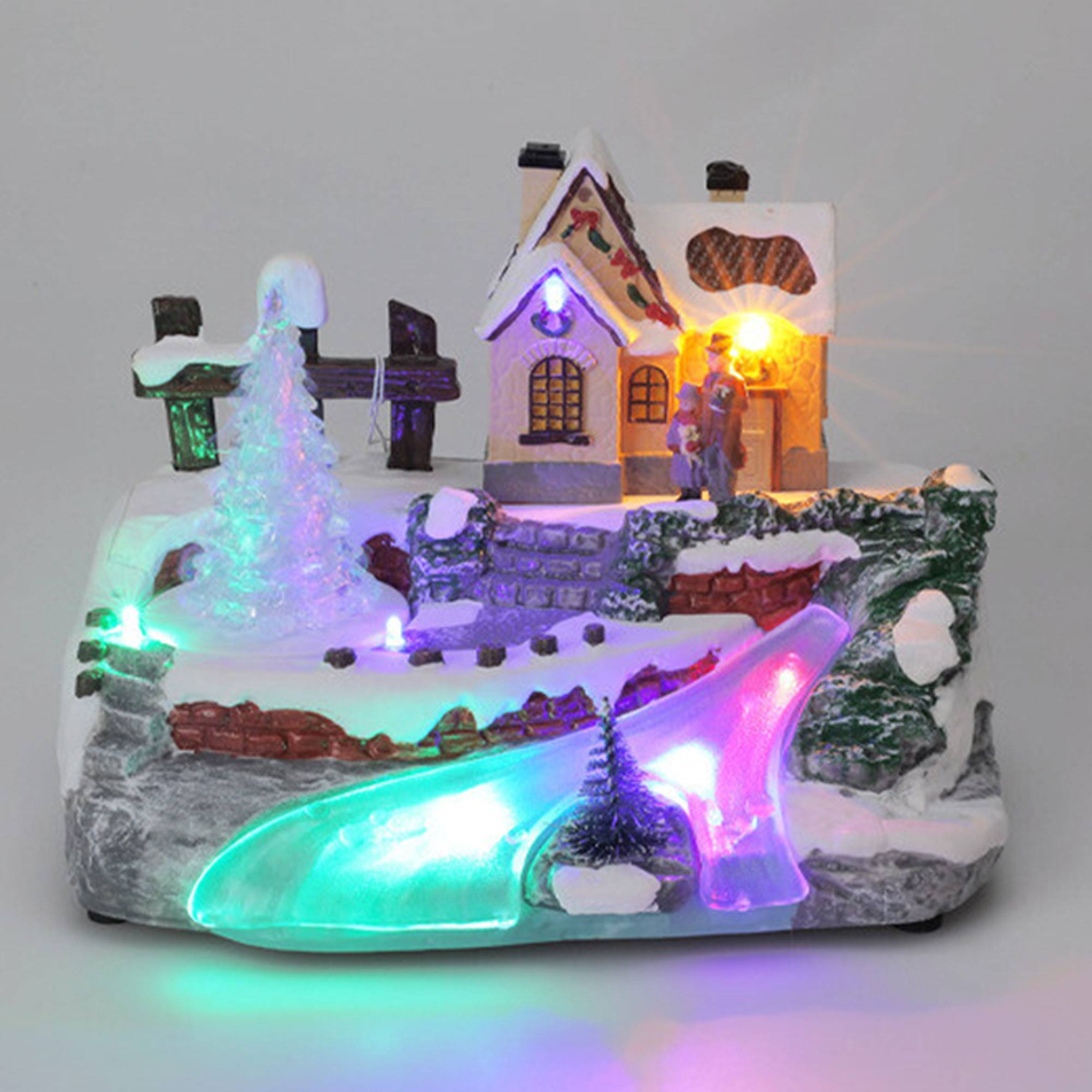 Una escena navideña en miniatura con una casa, una valla, un puente y un camino brillante. Tiene luces de colores.