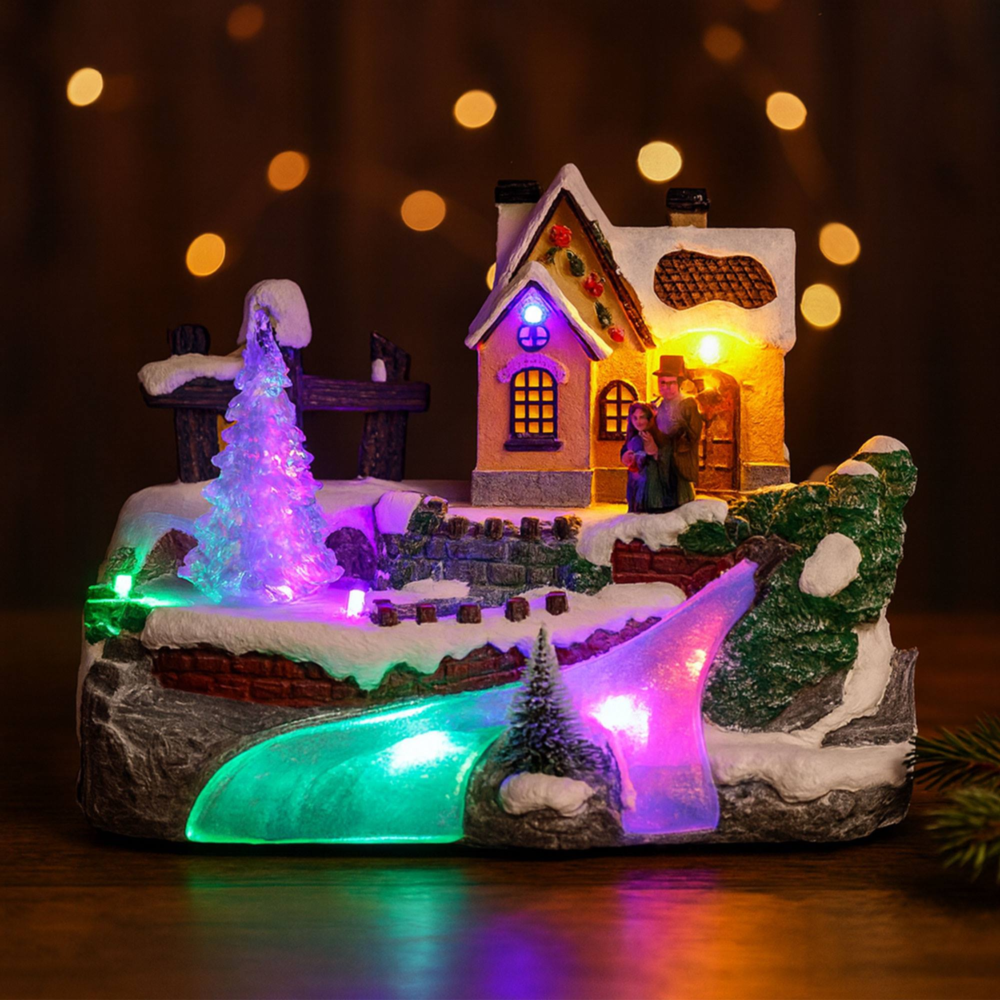 Una escena de pueblo navideño con una casa, figuras, árboles y luces. También se ven nieve y un río iluminado.
