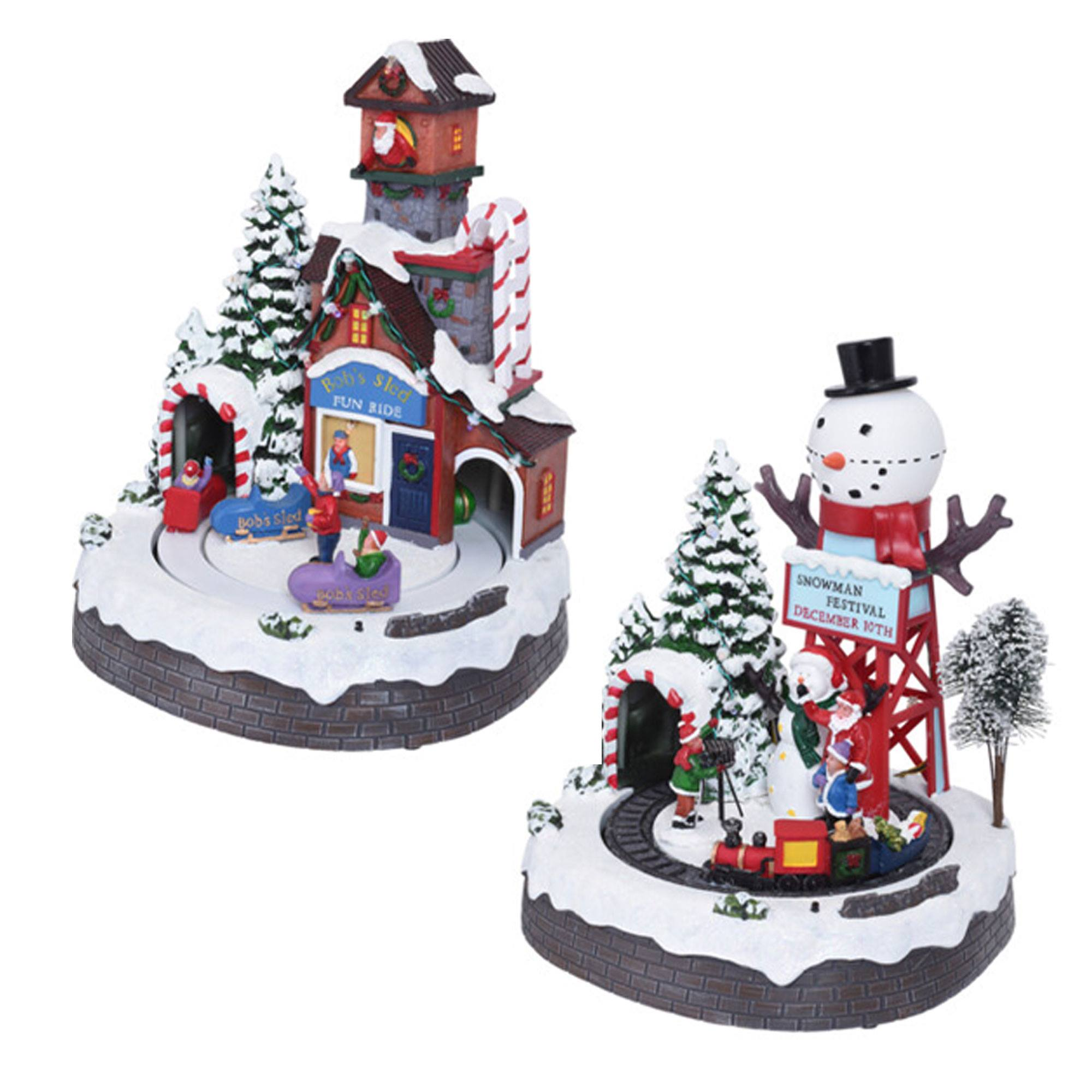 Dos decoraciones navideñas de pueblo. Una tiene una atracción divertida, la otra un muñeco de nieve. Ambas están sobre una base nevada.