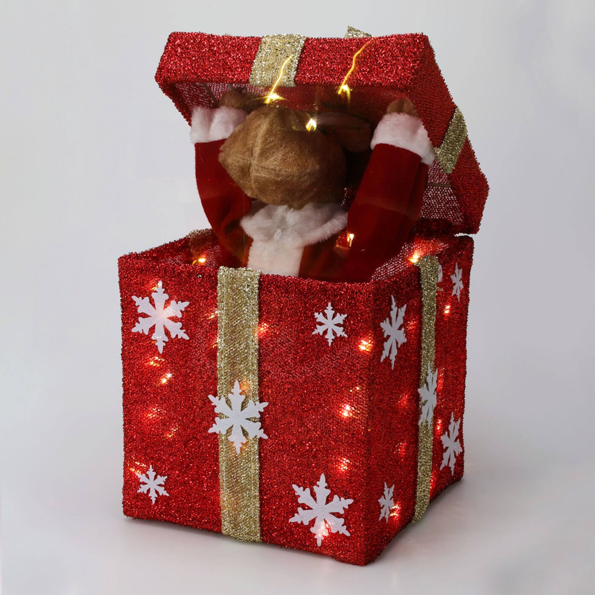 Una caja de regalo roja brillante con una figura de Papá Noel que sale. La caja tiene copos de nieve y rayas doradas. Luces en el interior.
