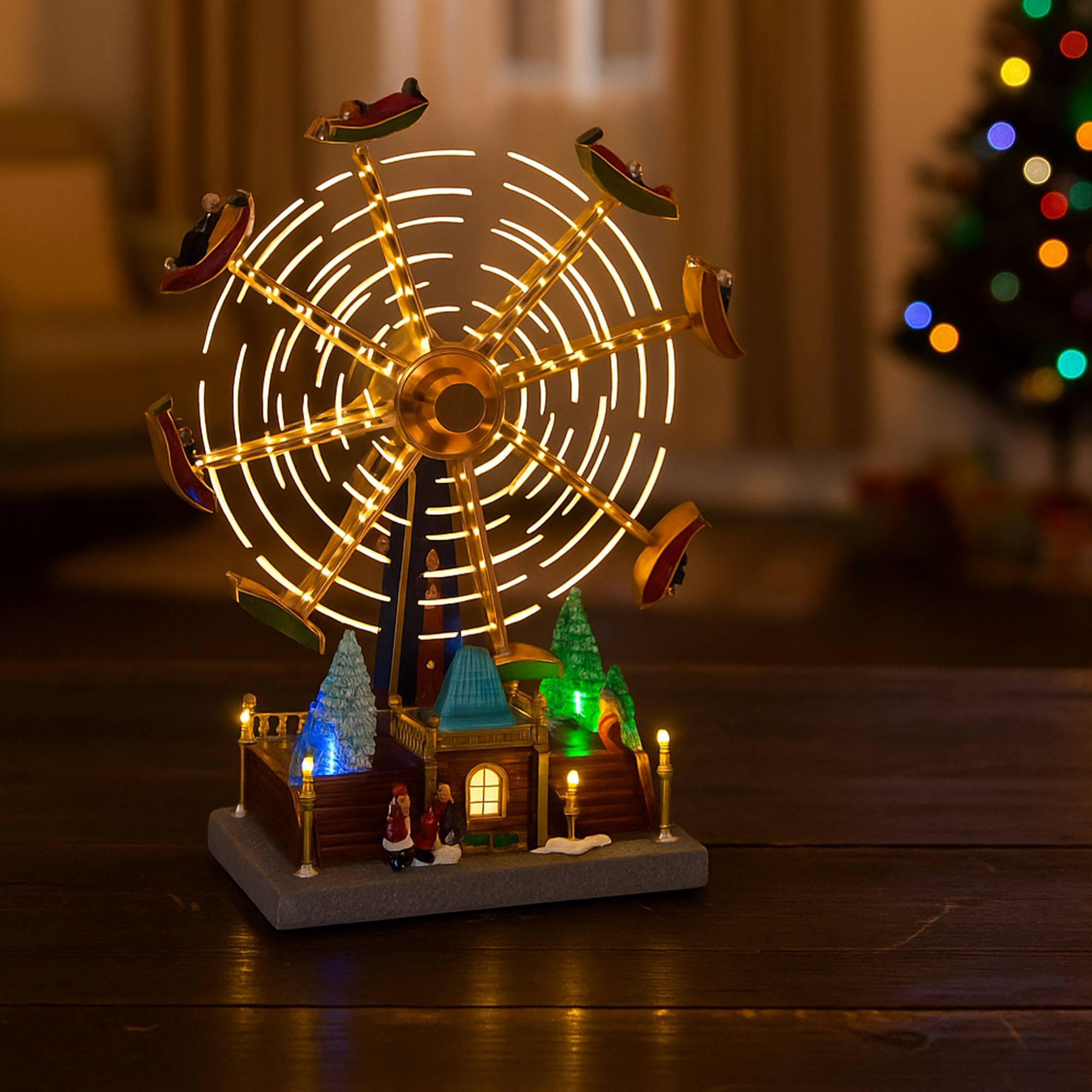Un modelo iluminado de noria navideña con gente en los coches, árbol de Navidad al fondo. Las luces están encendidas.