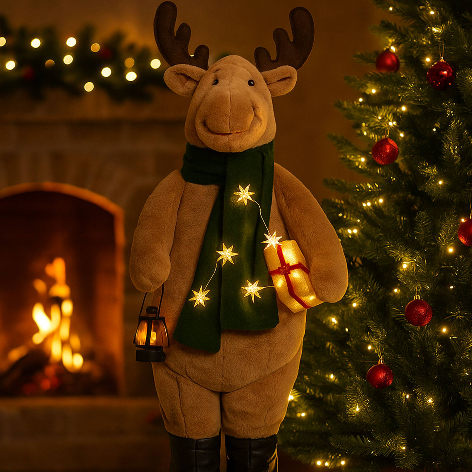 Una figura de reno con bufanda verde, linterna y regalo, de pie junto a un árbol de Navidad.