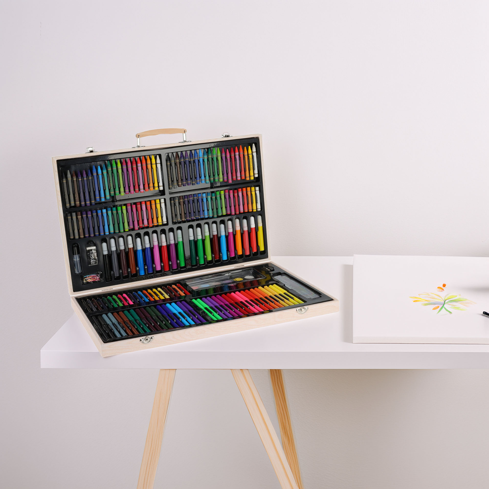 Juego de arte de madera sobre una mesa blanca. Abierto, mostrando crayones, marcadores y pasteles. Un dibujo de una flor está a la derecha.