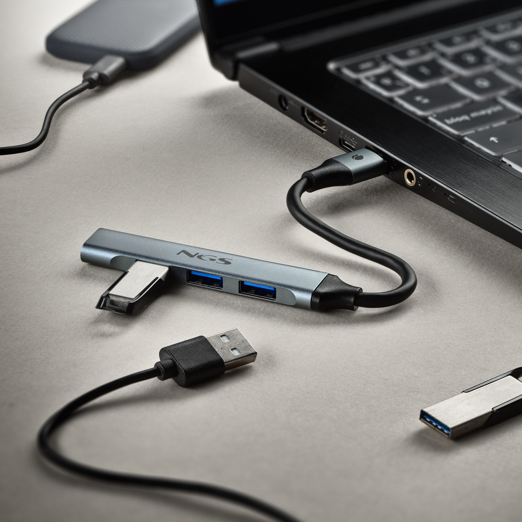 Ein Laptop, der mit einem USB-Hub, einer tragbaren Festplatte und USB-Sticks verbunden ist, alles auf grauem Grund.