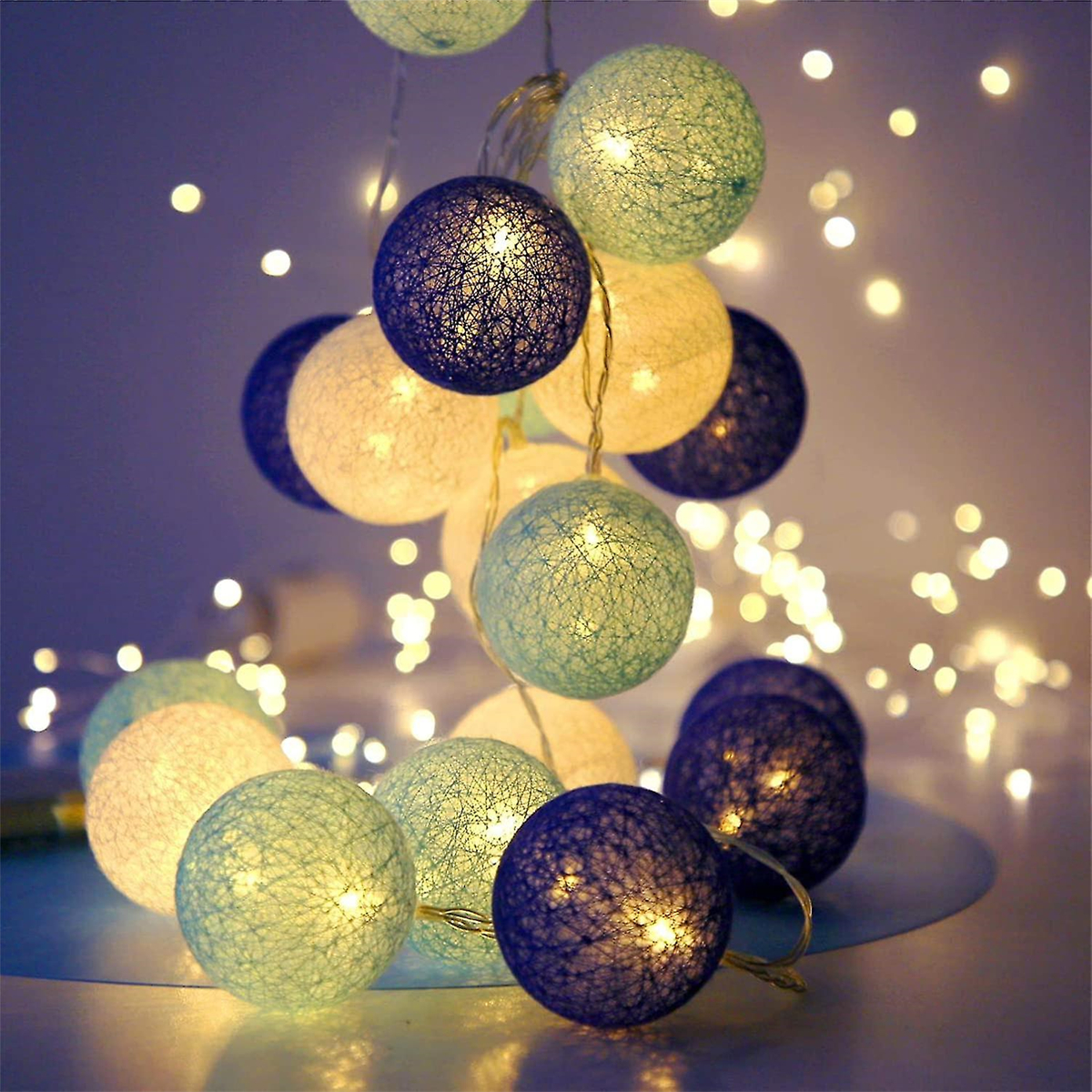 Lichterketten mit blauen, grünen und cremefarbenen Kugeln. Der Hintergrund ist mit Bokeh-Lichtern verschwommen, was eine weiche, warme Atmosphäre schafft.