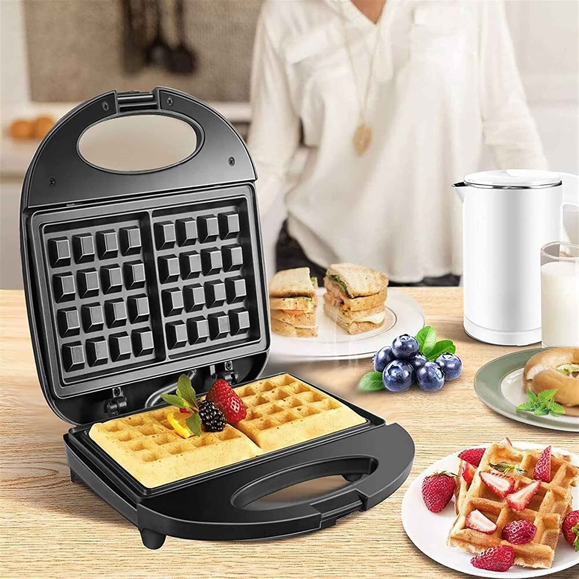 Offener Waffeleisen mit Waffeln. Weitere Teller zeigen Sandwiches, Blaubeeren und Waffeln mit Erdbeeren.
