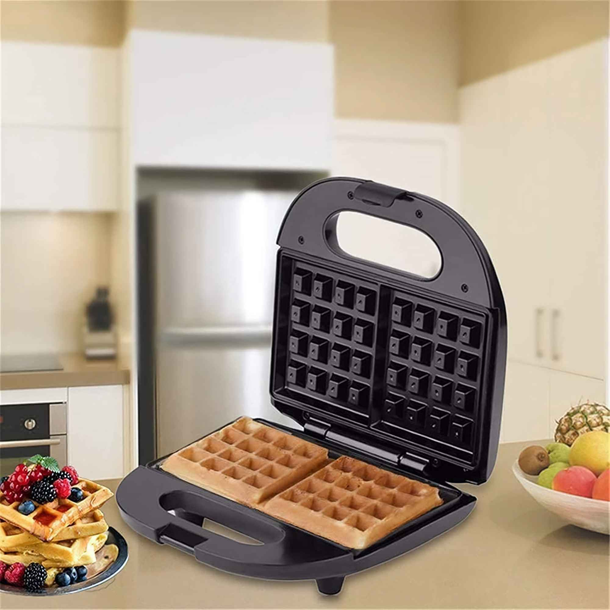 Ein Waffeleisen mit zwei Waffeln. Beeren auf Waffeln auf einem Teller. Früchte in einer Schüssel auf einer Küchenzeile.
