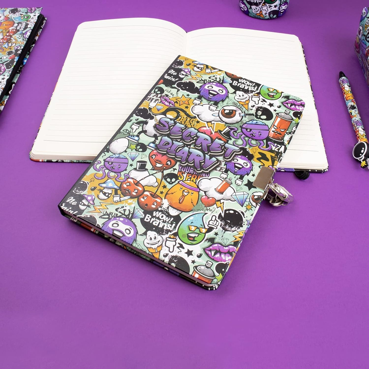 Ein buntes Tagebuch mit Schloss liegt offen auf einer violetten Oberfläche. Andere Schreibwaren mit ähnlichen Graffiti-Designs umgeben es.