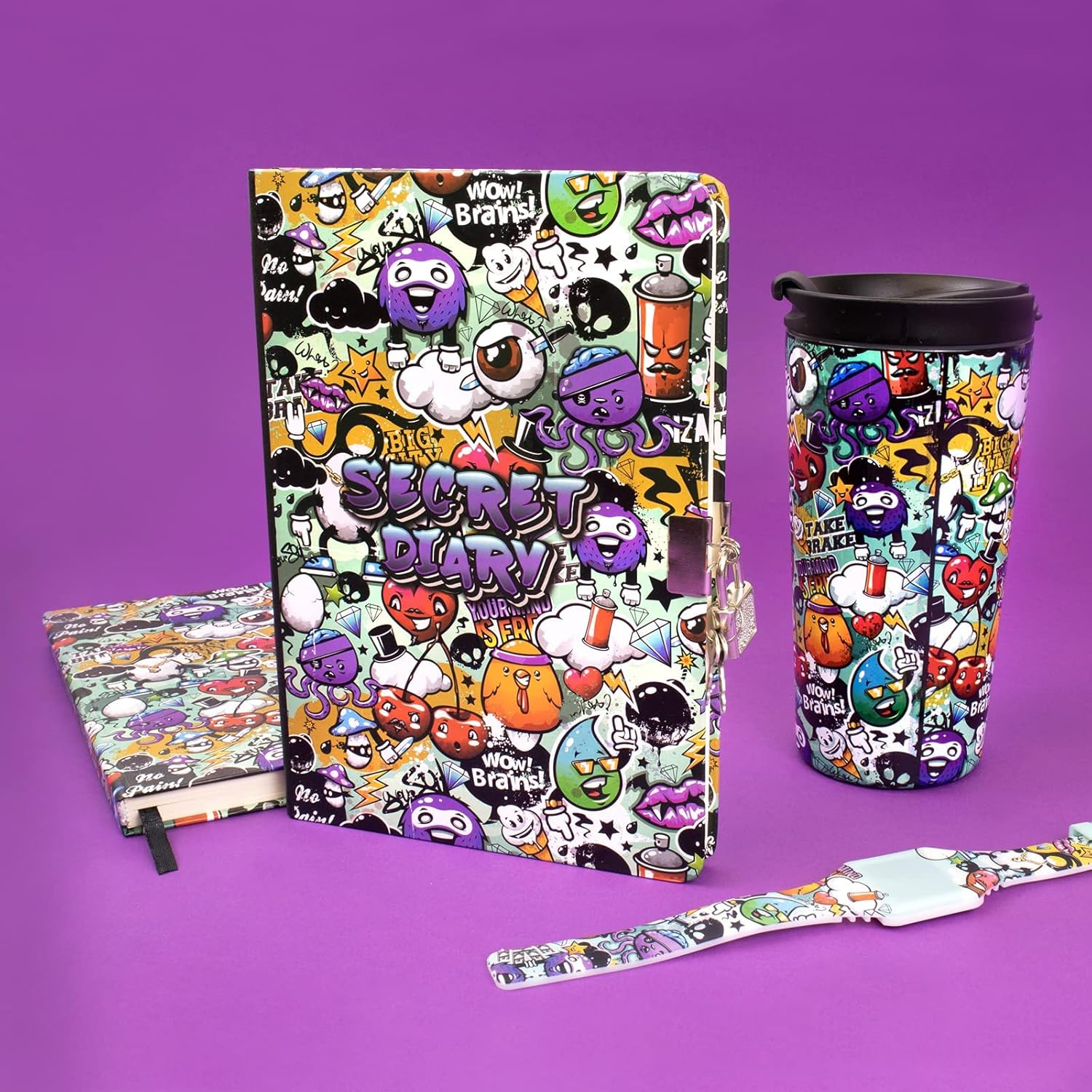 Auf lila Hintergrund liegen ein Tagebuch, ein Notizbuch, ein Reisebecher und ein Armband mit Graffiti-Illustrationen.