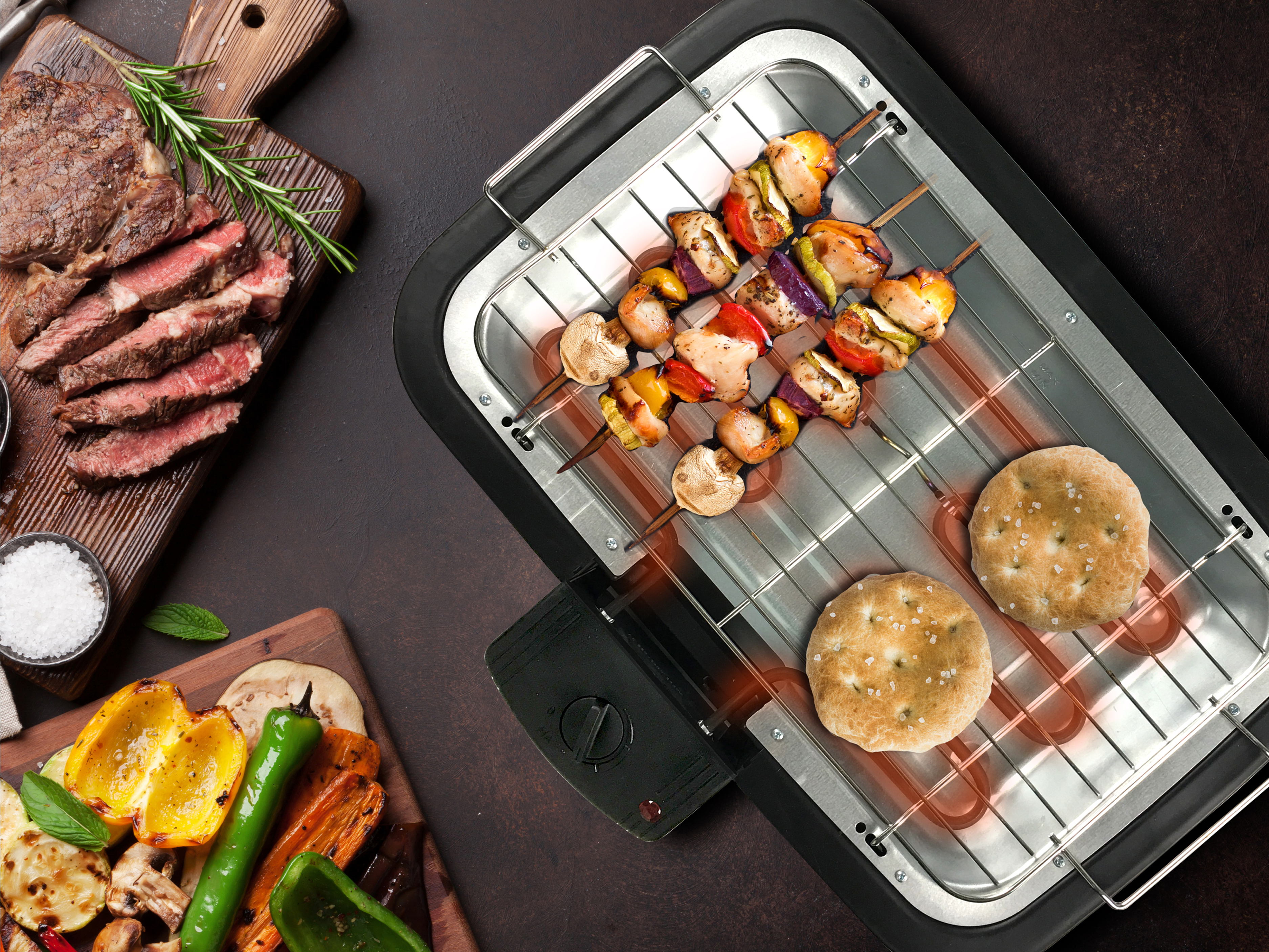 Grillowane jedzenie: stek, szaszłyki, chleb i grillowane warzywa na ciemnej powierzchni.