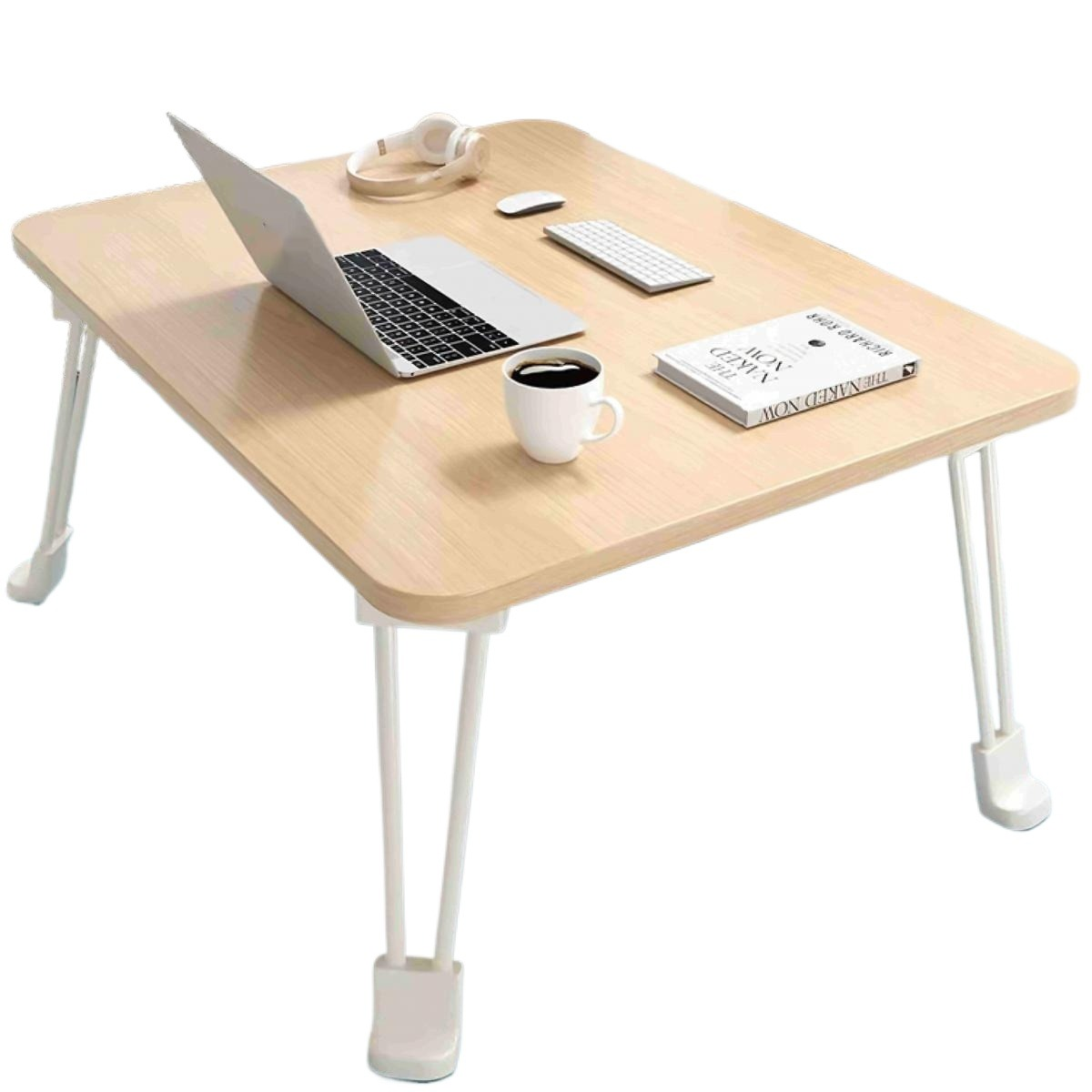 Auf einem hellen Holztisch mit weißen Beinen liegen ein Laptop, Kopfhörer, eine Maus, eine Tastatur, eine Kaffeetasse und ein Buch.