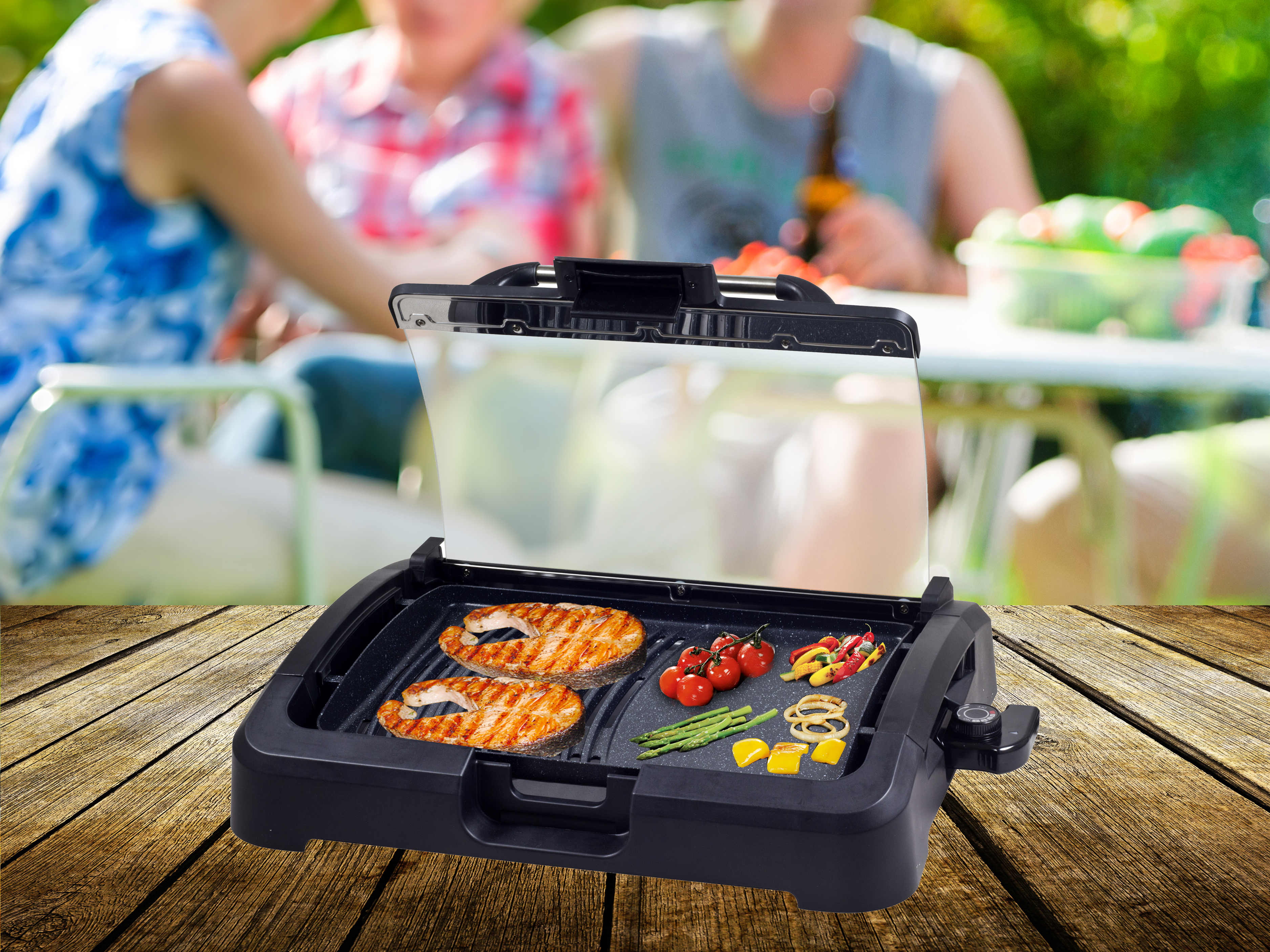 Auf einem Holztisch steht ein Grill mit Lachs, Tomaten und Paprika. Im Hintergrund sind Leute zu sehen.