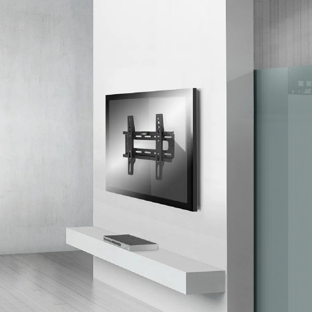 Un soporte de pared para TV está fijado a una pared blanca. Un televisor está montado sobre él. Debajo hay una estantería blanca con un reproductor de DVD negro.