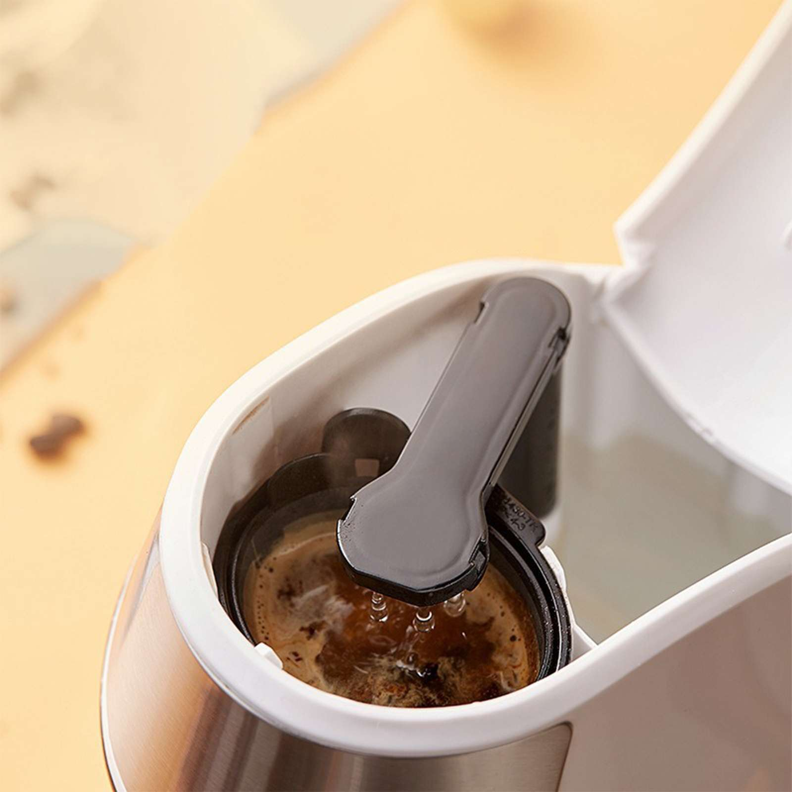 Kaffeemaschine mit Kaffeezubereitung. Wasser tropft in den Kaffeefilter. Weiße und graue Maschine auf beigefarbener Oberfläche.