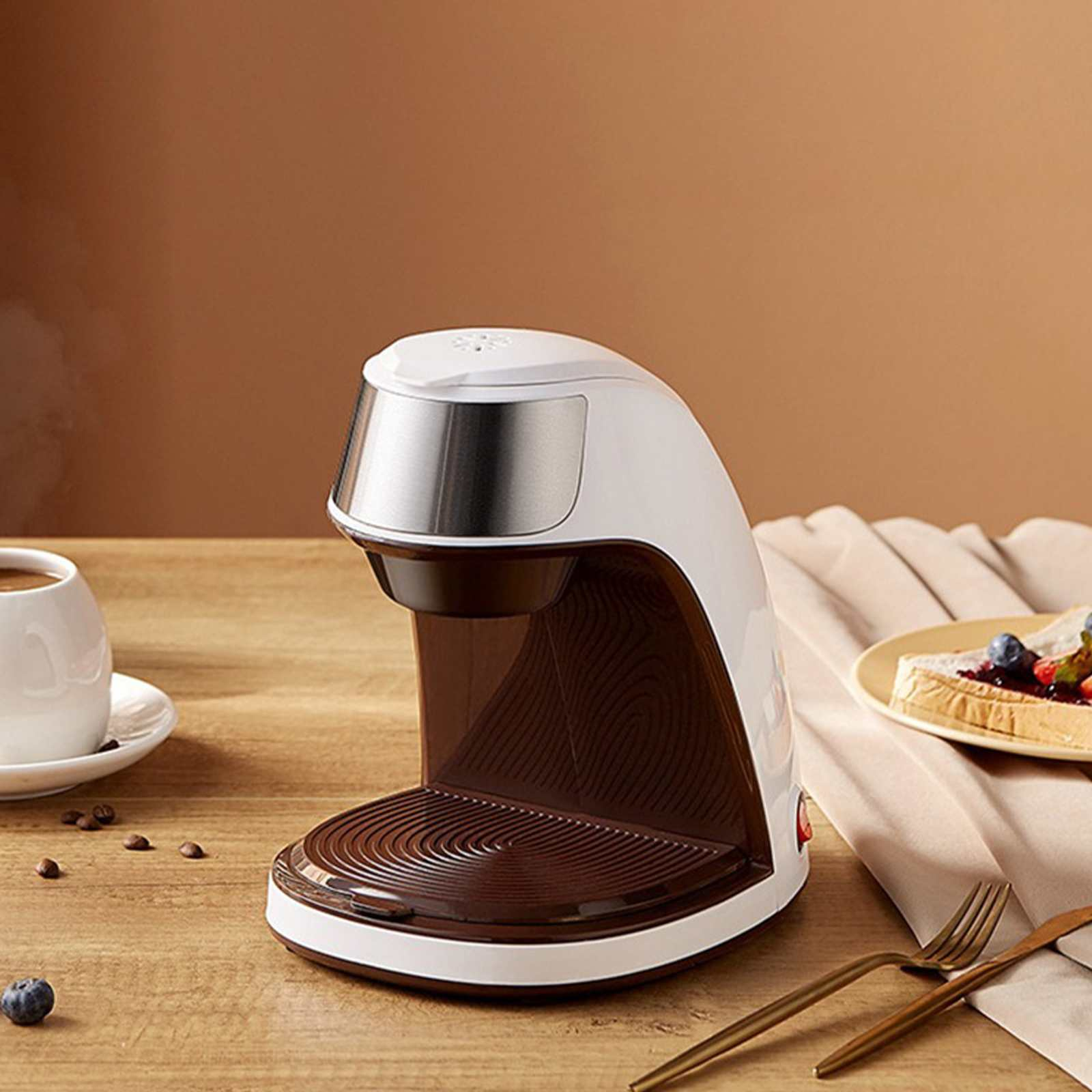 Eine weiß-braune Kaffeemaschine auf einem Holztisch. Es gibt eine Tasse Kaffee, Toast und Besteck.