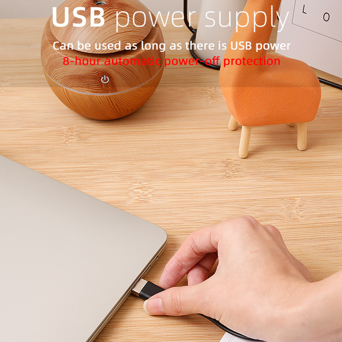 Eine Hand steckt ein USB-Kabel in einen Laptop. Ein hölzerner Luftbefeuchter und ein orangefarbenes hirschförmiges Objekt stehen auf einem Holztisch.