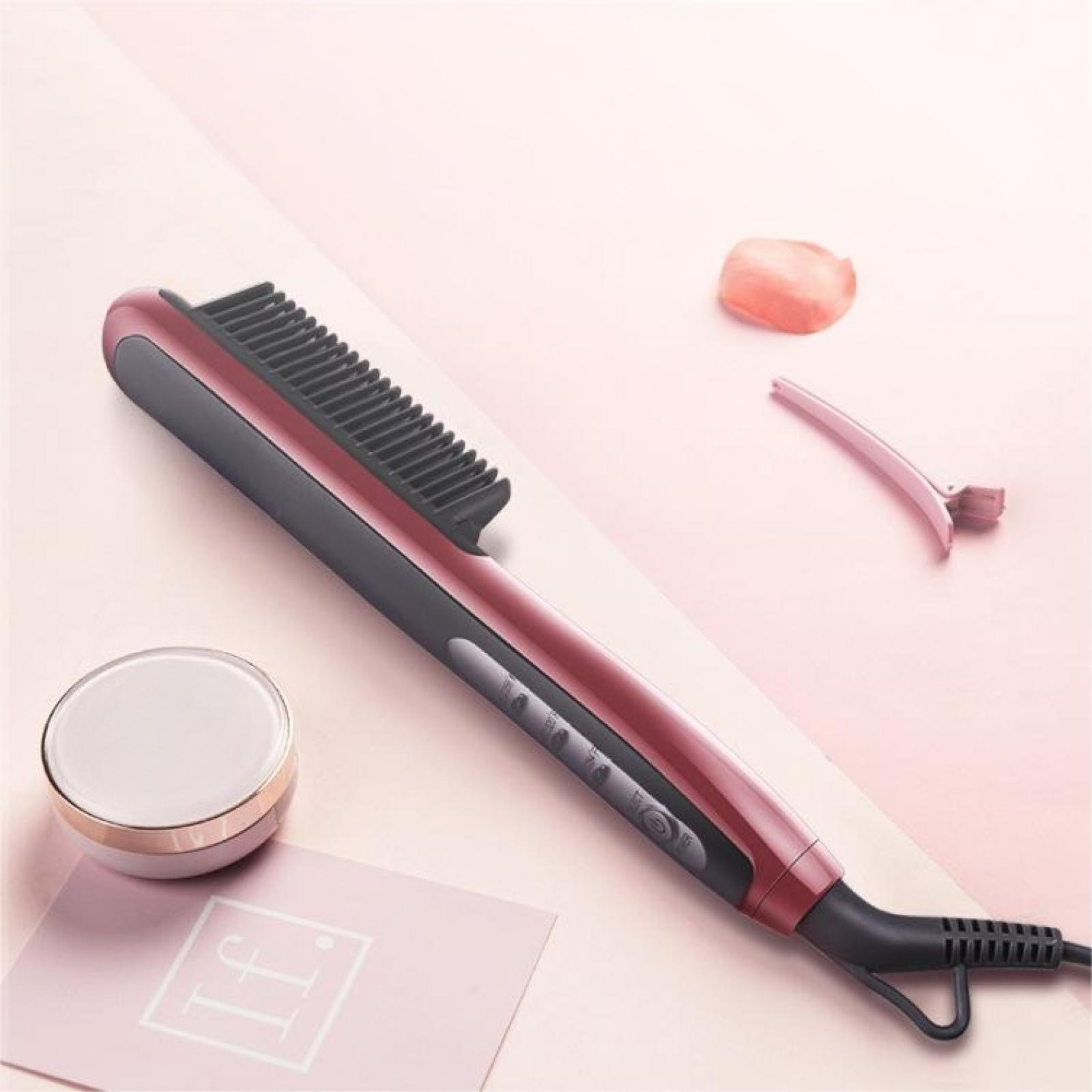 Ein roter und schwarzer Haarglätter, eine rosa Haarspange, ein Kosmetikglas und eine rosa Karte liegen auf einer rosa Oberfläche.