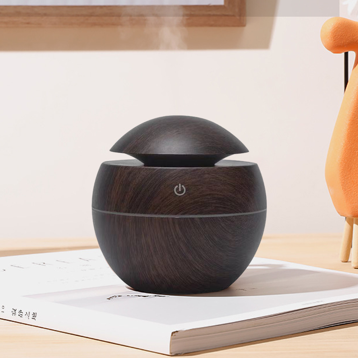 Ein Diffusor aus dunklem Holzmaserung steht auf einem Buch. Dampf steigt auf. Ein orangefarbenes Deko-Stück ist im Hintergrund.