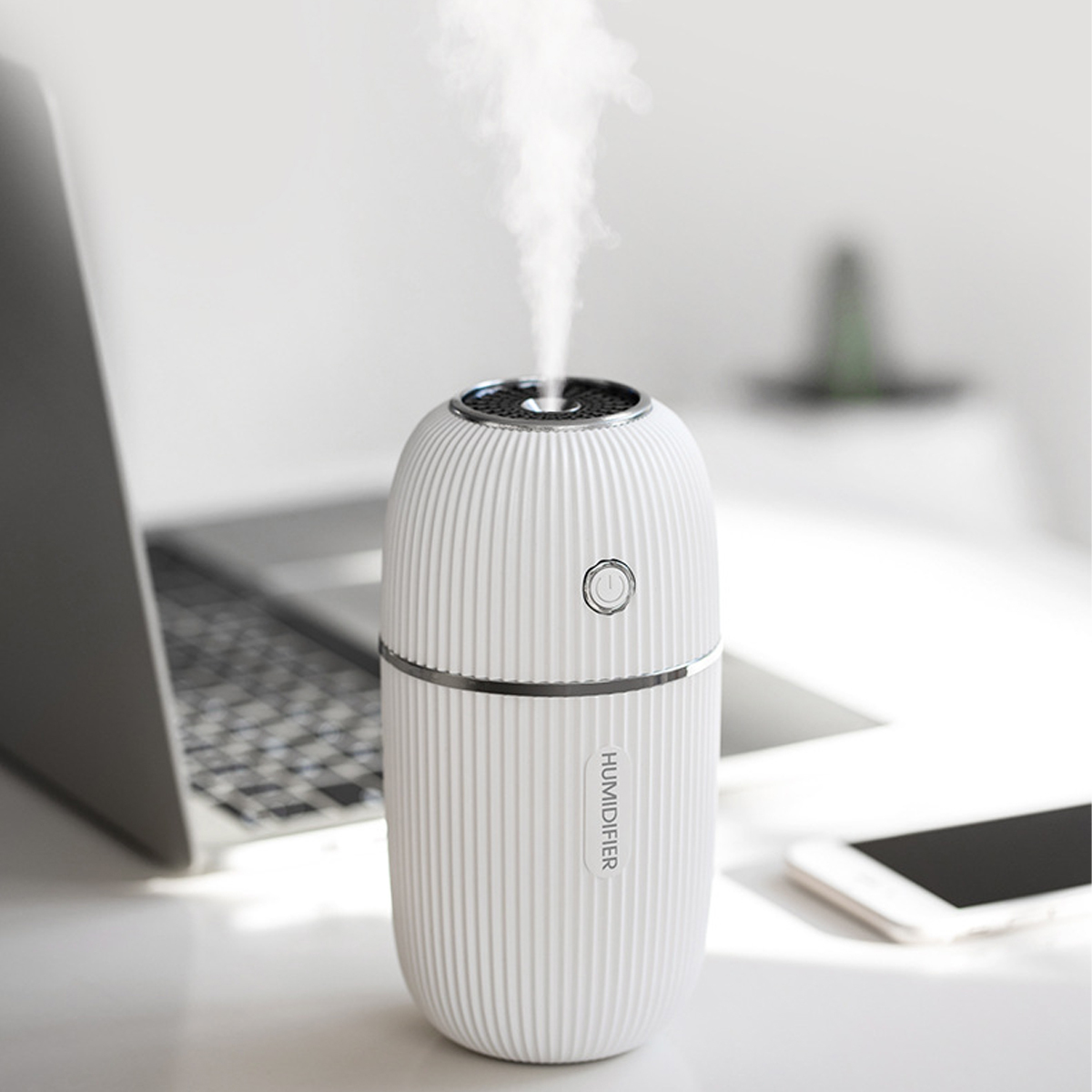 Ein weißer Luftbefeuchter gibt Dampf ab. Er steht auf einem Schreibtisch mit Laptop und Telefon. Das Wort HUMIDIFIER ist sichtbar.
