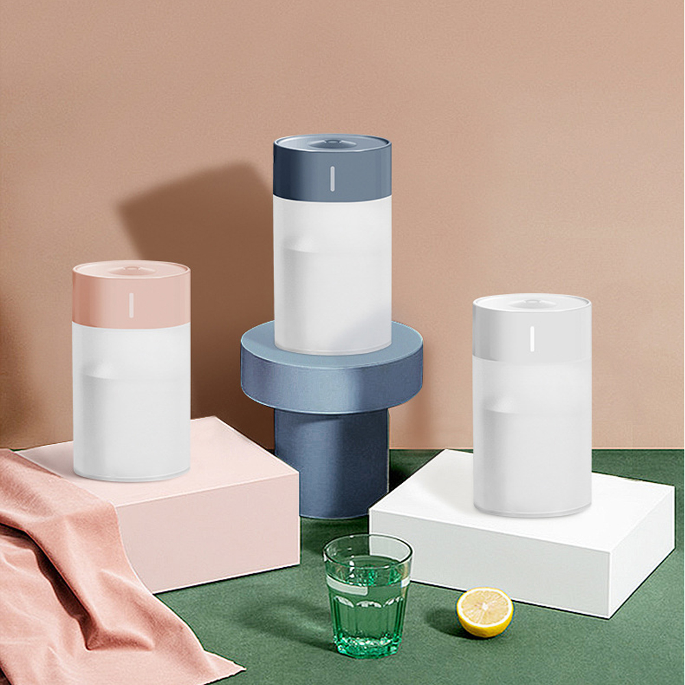 Drei zylindrische Luftbefeuchter mit farbigen Deckeln auf geometrischen Plattformen. Ein Glas Wasser und eine Zitronenscheibe im Vordergrund.